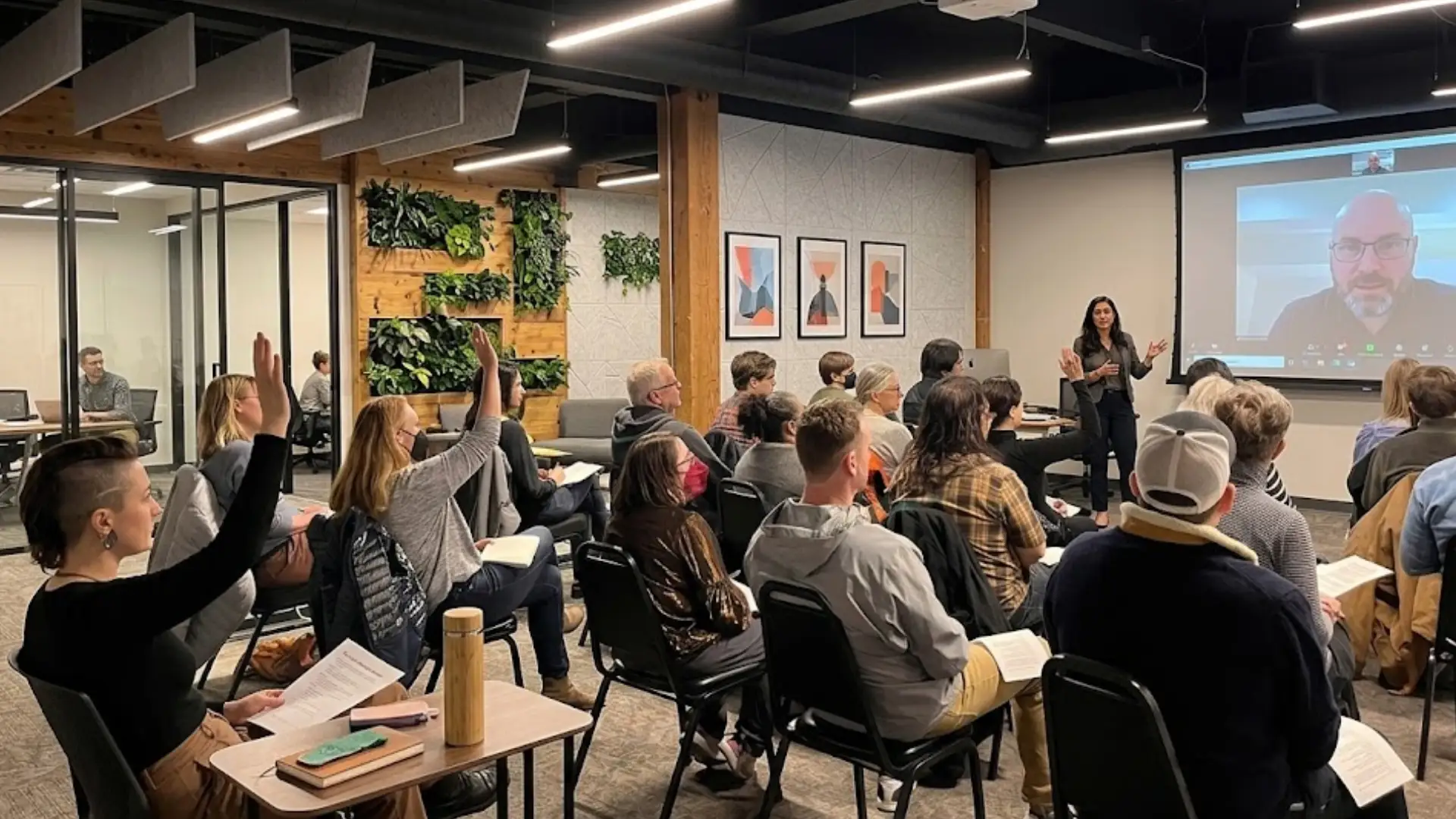 Audience attending workshop or class, raising hands while speaker presents on screen in modern space