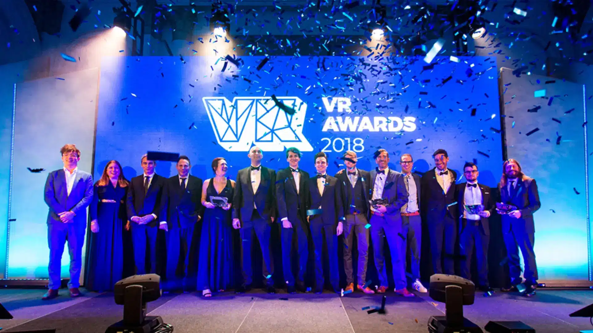 Award ceremony stage with winners in formal attire celebrating under lights and confetti during event