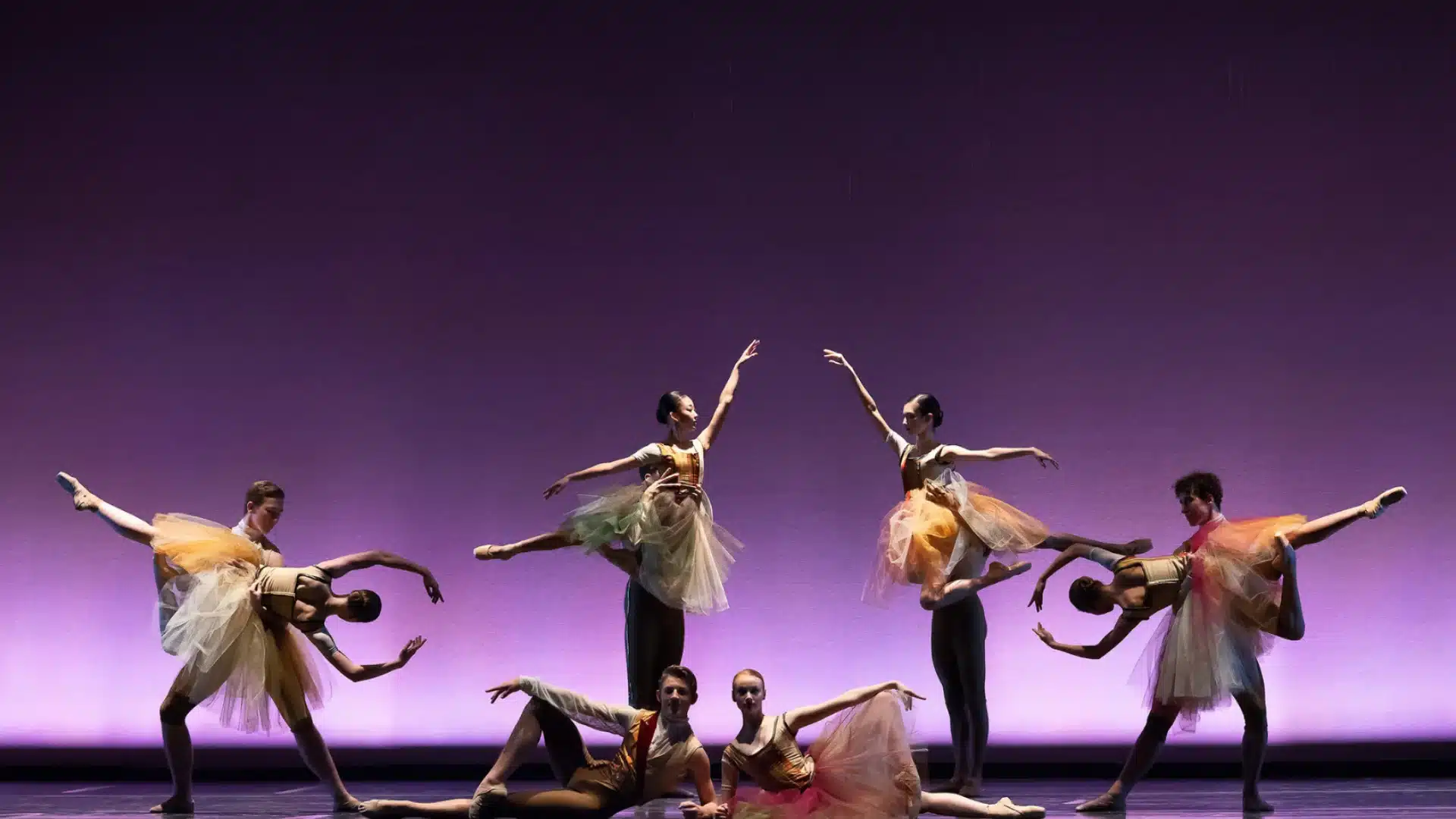 Ballet dancers performing synchronized routine on stage with dramatic lighting and elegant costumes