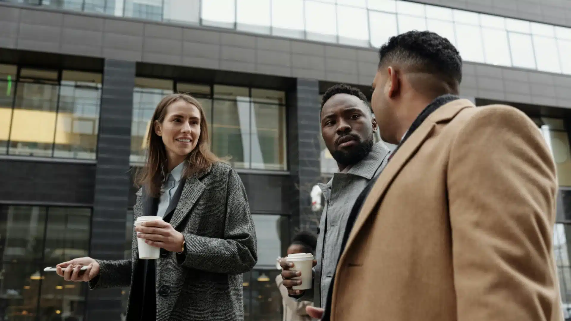 Colleagues chatting outdoors with coffee cups during casual networking break near office building