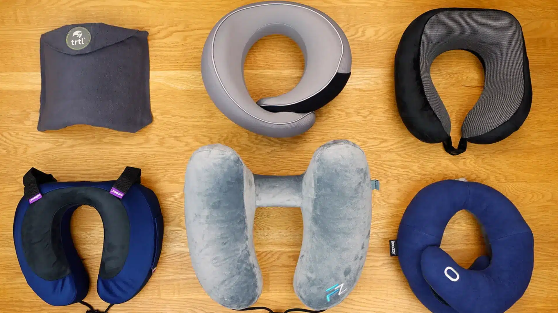 Collection of ergonomic travel neck pillows in different shapes and fabrics arranged on wooden surface