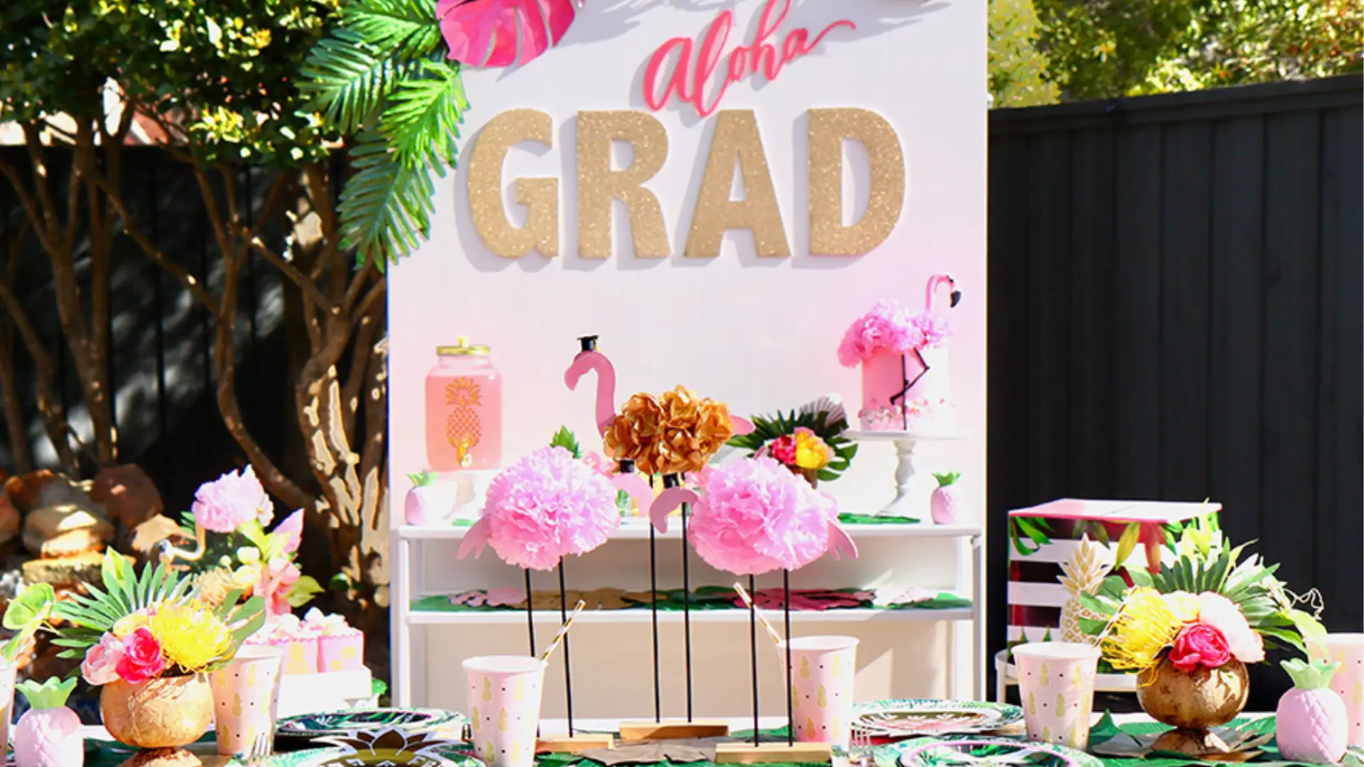 Colorful graduation party setup with “Grad” sign, tropical decor, balloons, and festive table arrangements