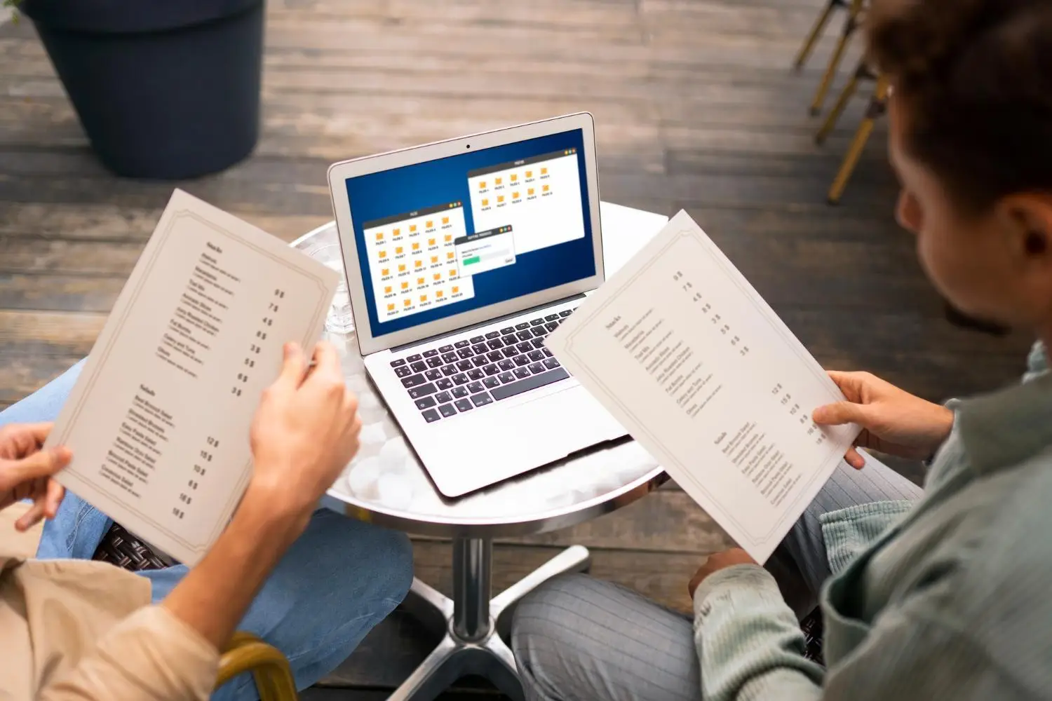 Two people reviewing documents at a cafe table with open laptop