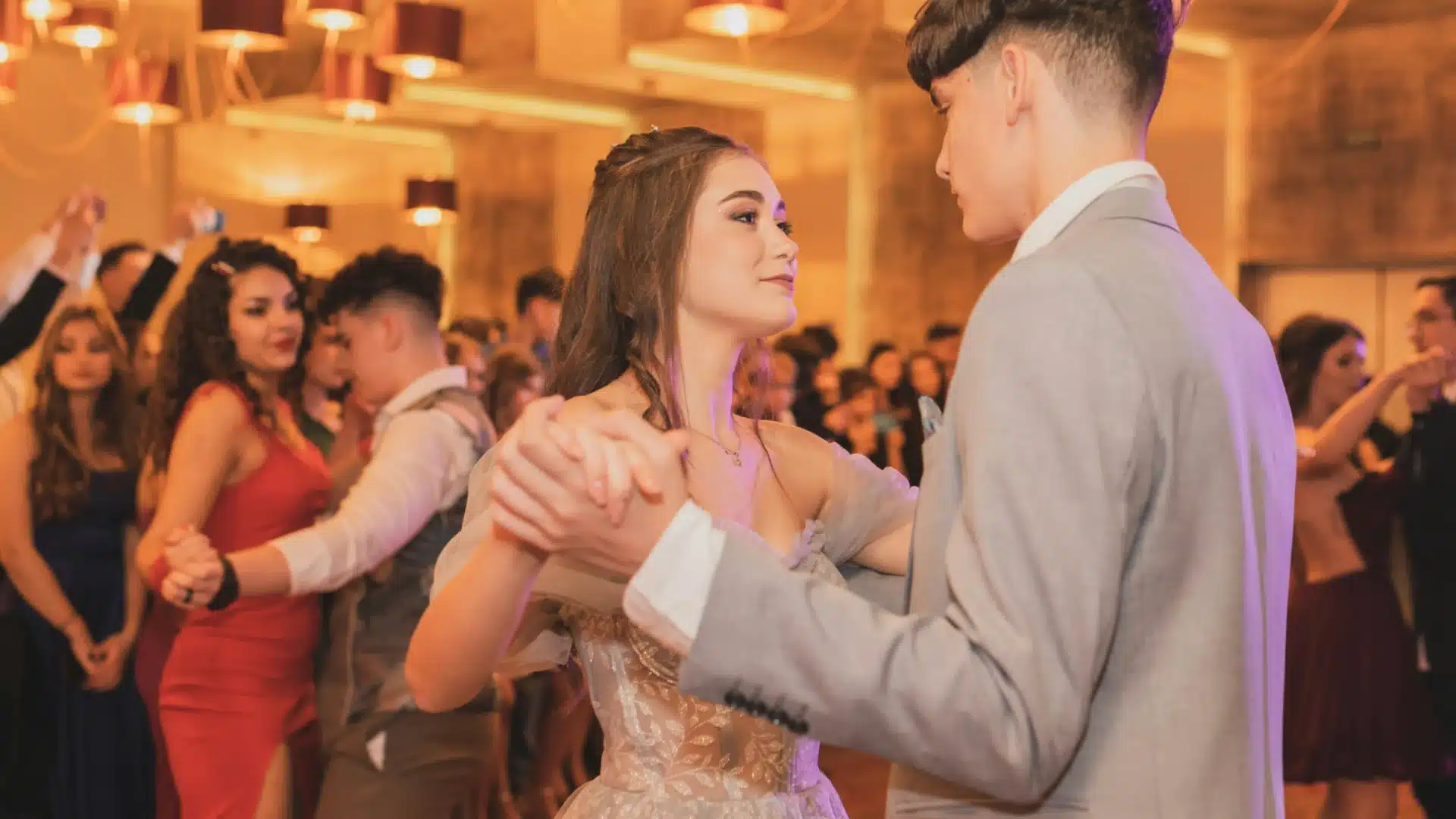 Couple dancing at formal gala event with guests in elegant attire and warm ambient lighting