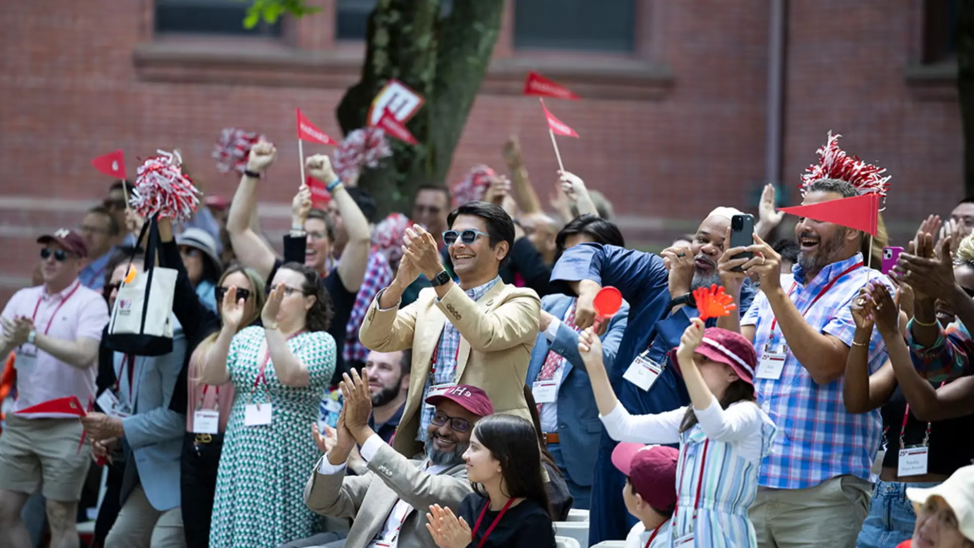 Crowd cheering and clapping at outdoor alumni gathering, celebrating school pride and reunion event