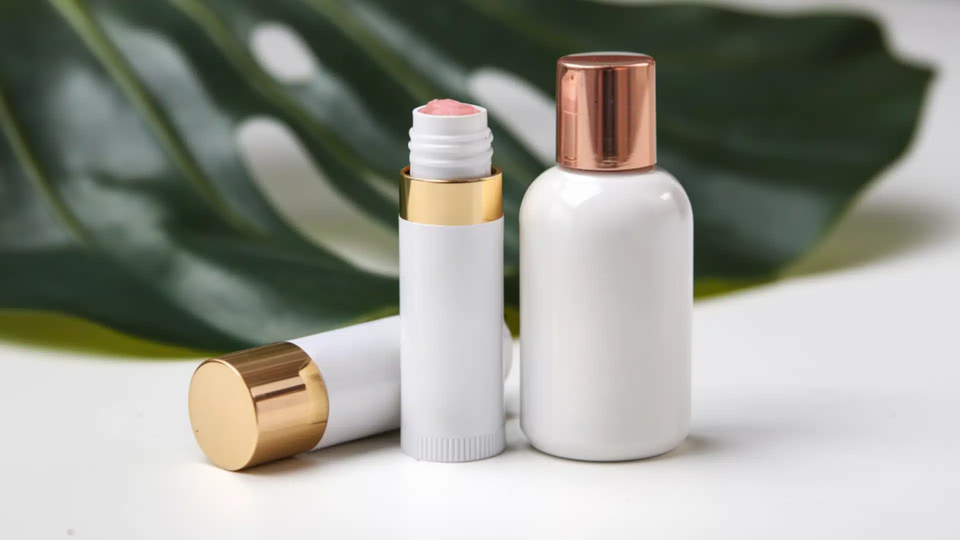 Custom lip balm tube and sunscreen bottle with gold caps placed on clean surface with green leaf background