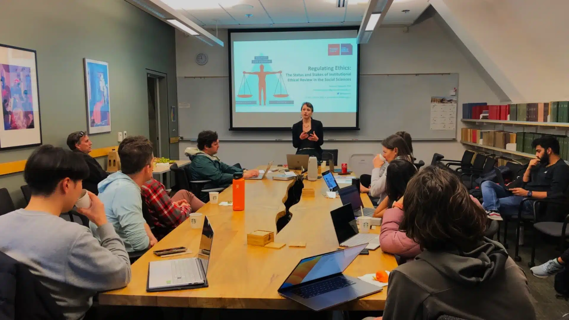 Educational seminar with presenter speaking to group around table using slides in classroom setting