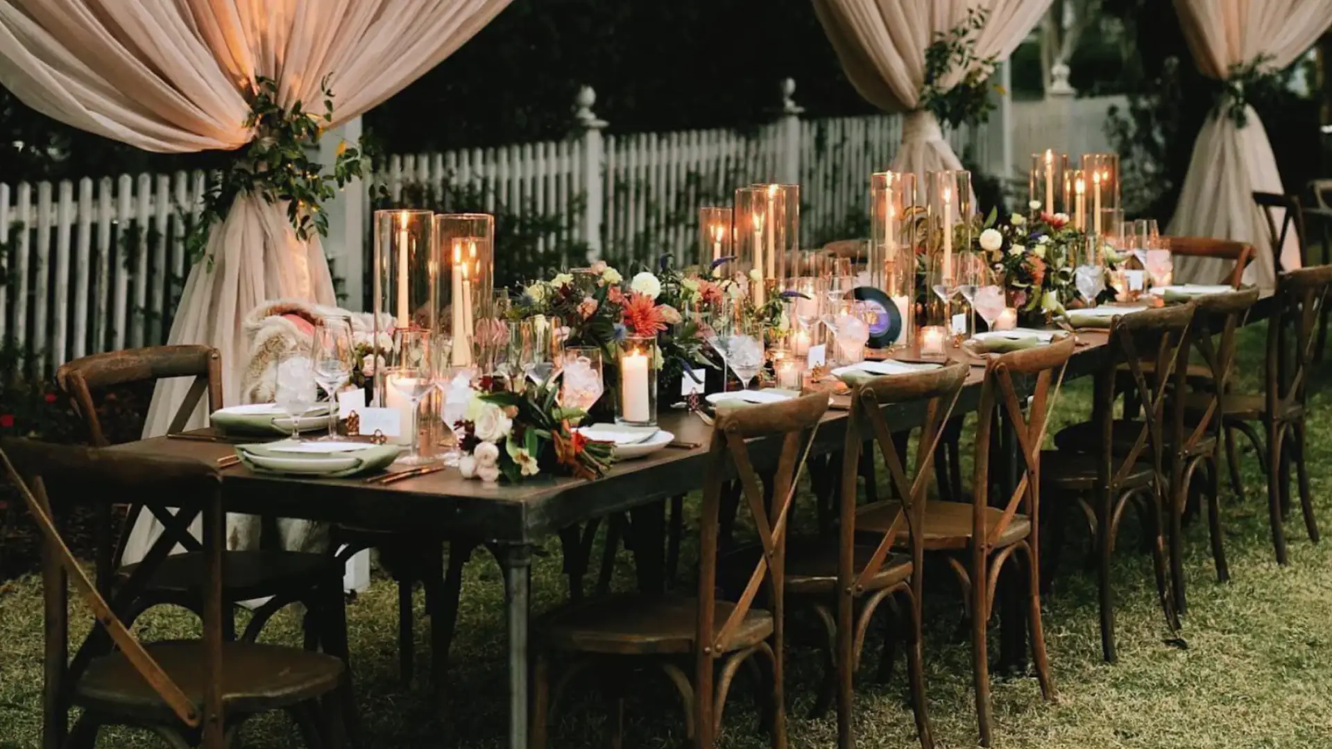 Elegant engagement party setup with long table, candles, floral decor, and draped outdoor evening ambiance