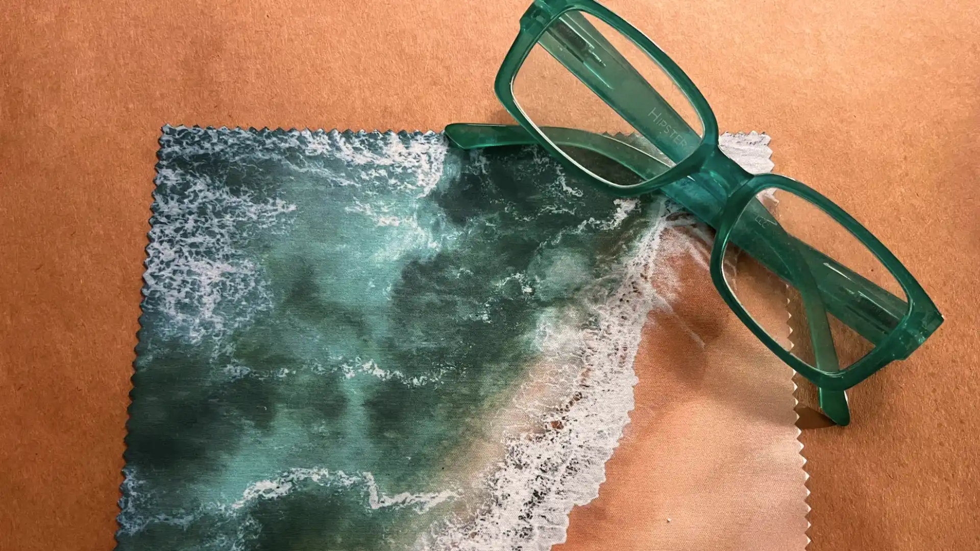 Eyeglasses resting on custom printed microfiber cloth featuring ocean waves design on textured surface