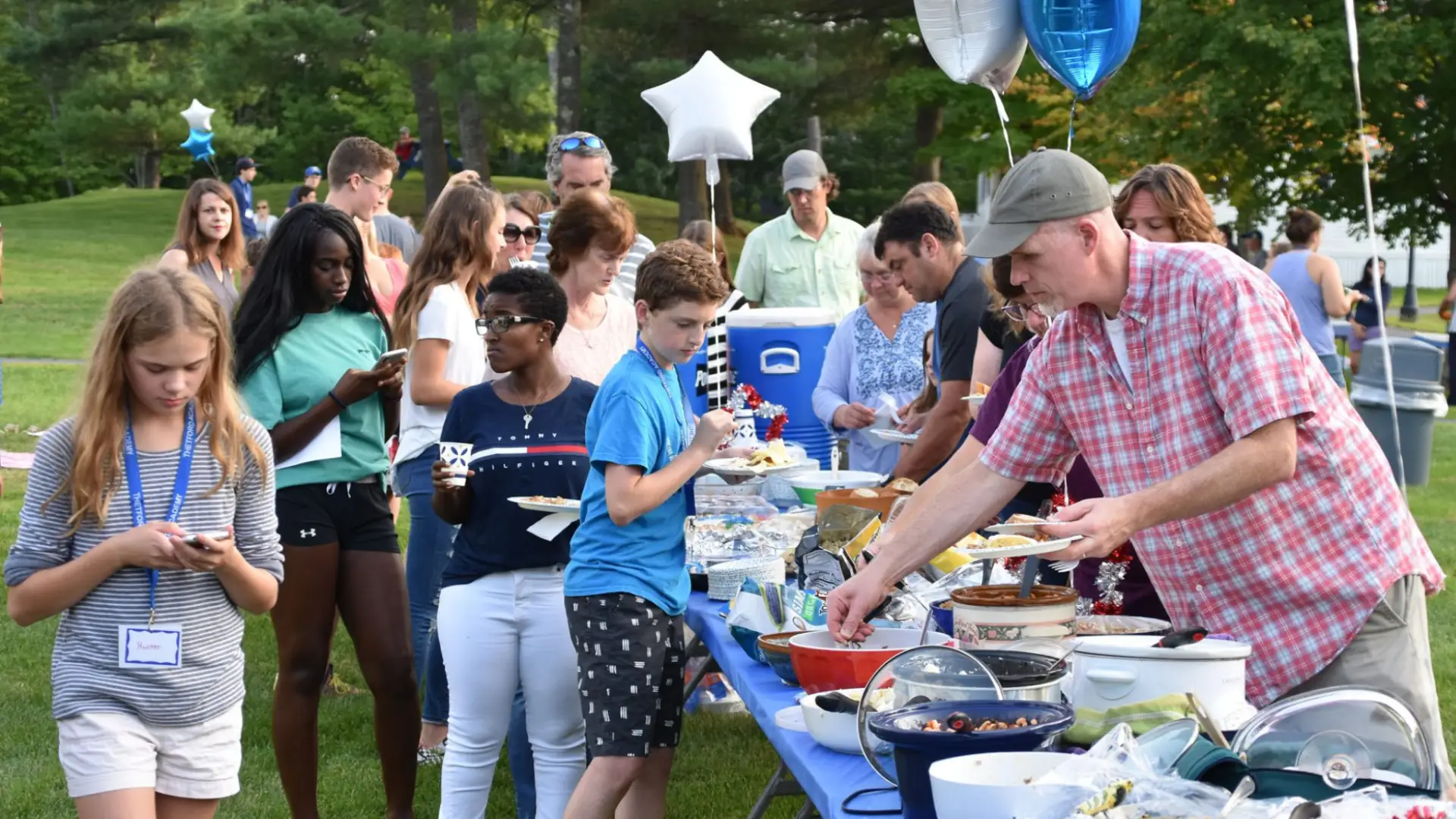 Families and students gathered outdoors at a school picnic, enjoying food, conversation, and a relaxed community atmosphere