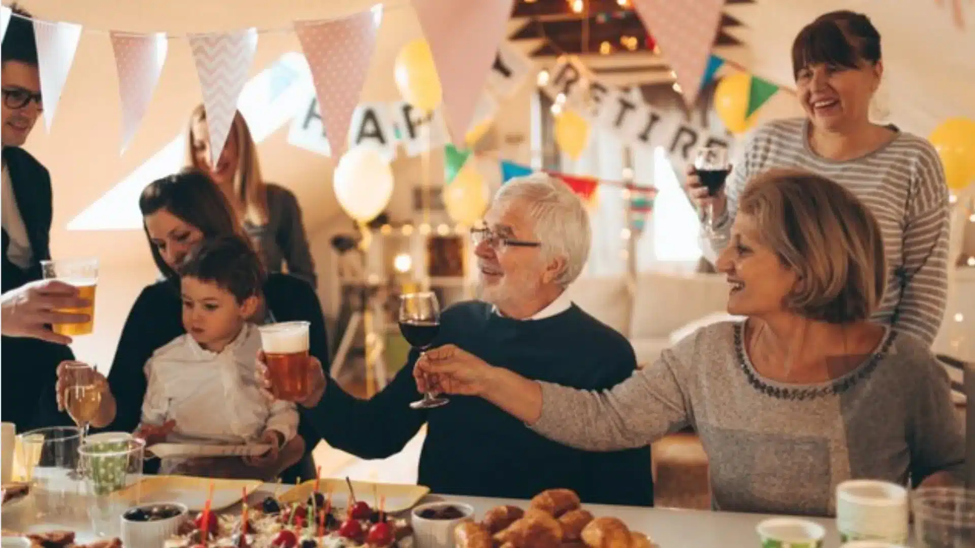 Family celebrating retirement party indoors with food, drinks, and decorations, sharing joyful moments together