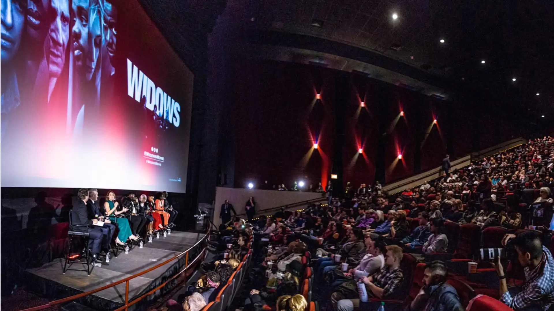 Film screening panel discussion in packed theater with audience watching speakers beneath large screen