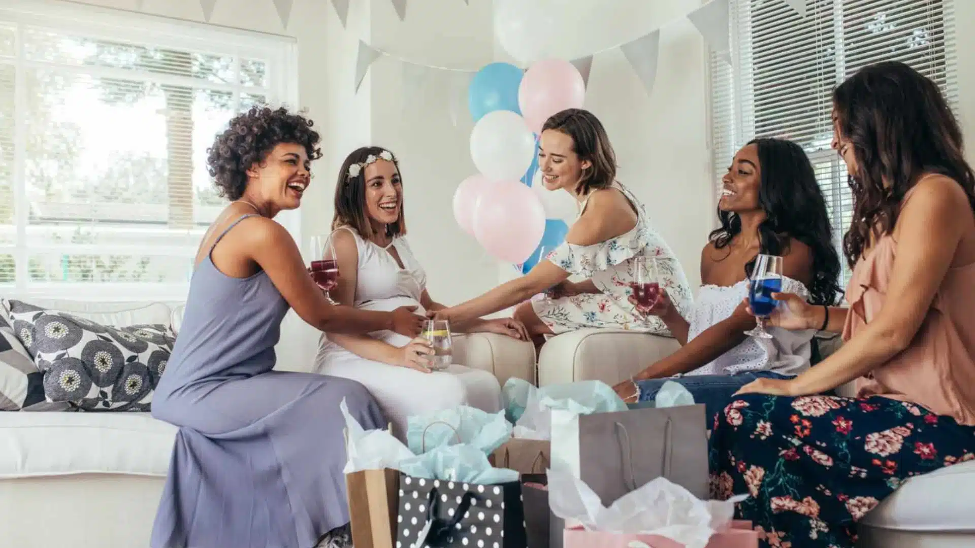 Friends celebrating baby shower with gifts, drinks, and decorations around expecting mother at home