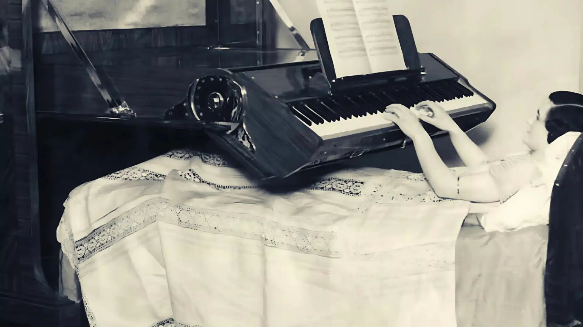 Vintage photo of bedridden woman playing piano mounted over bed with sheet music open above keyboard
