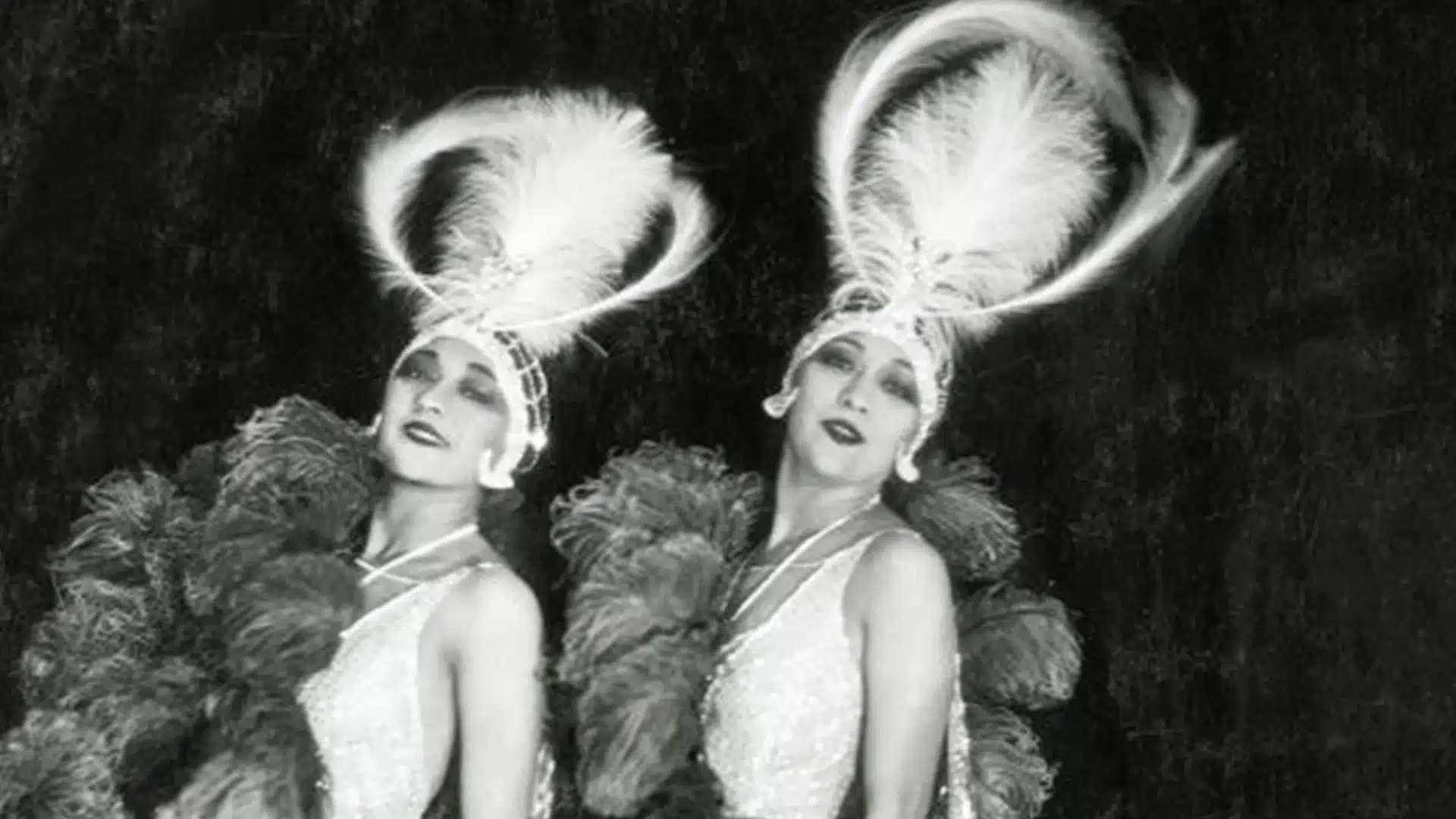Vintage photo of two women in glamorous costumes with feathered headpieces posing on stage together