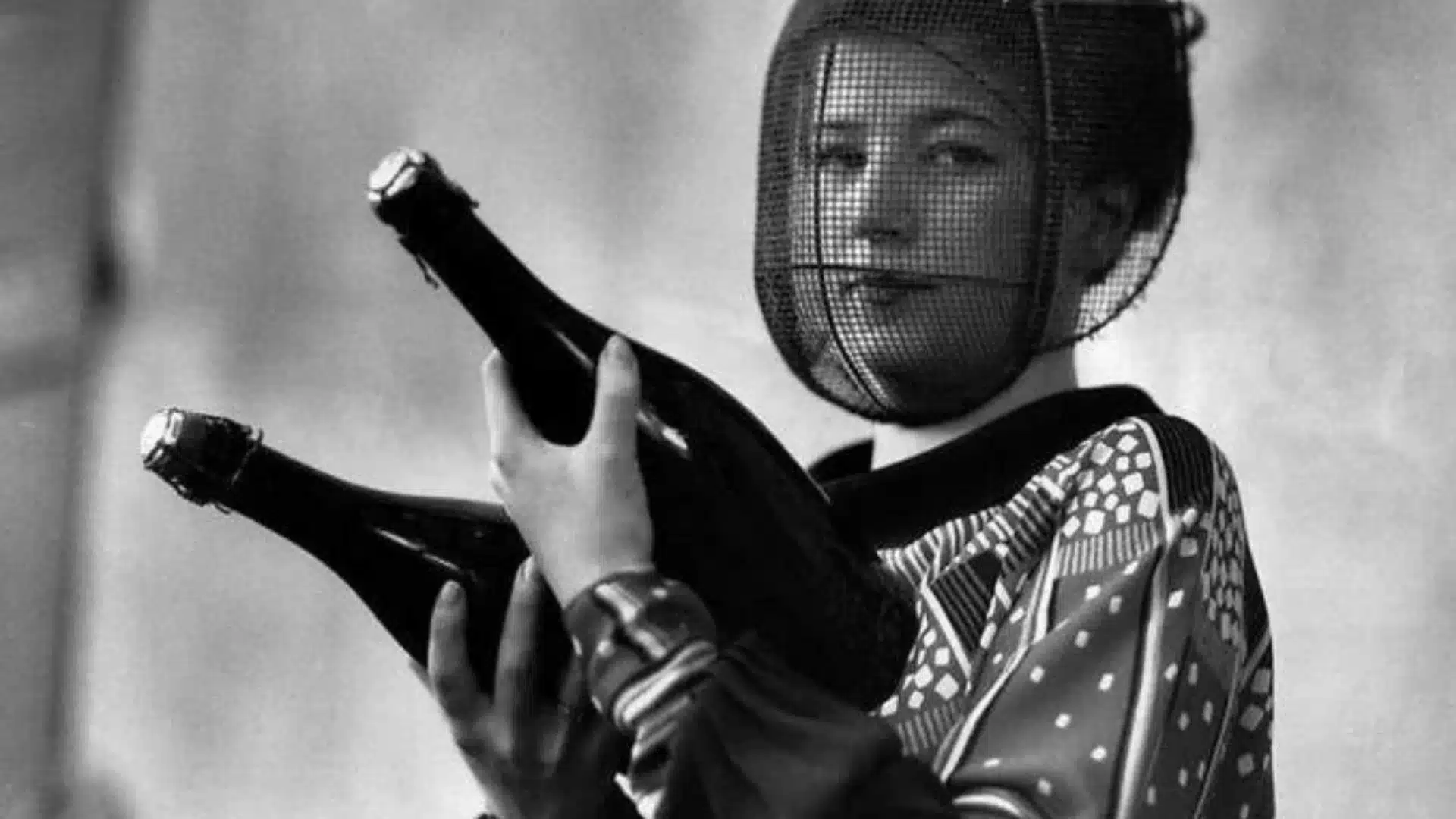 Black and white photo of woman wearing protective face mask holding two champagne bottles in hands