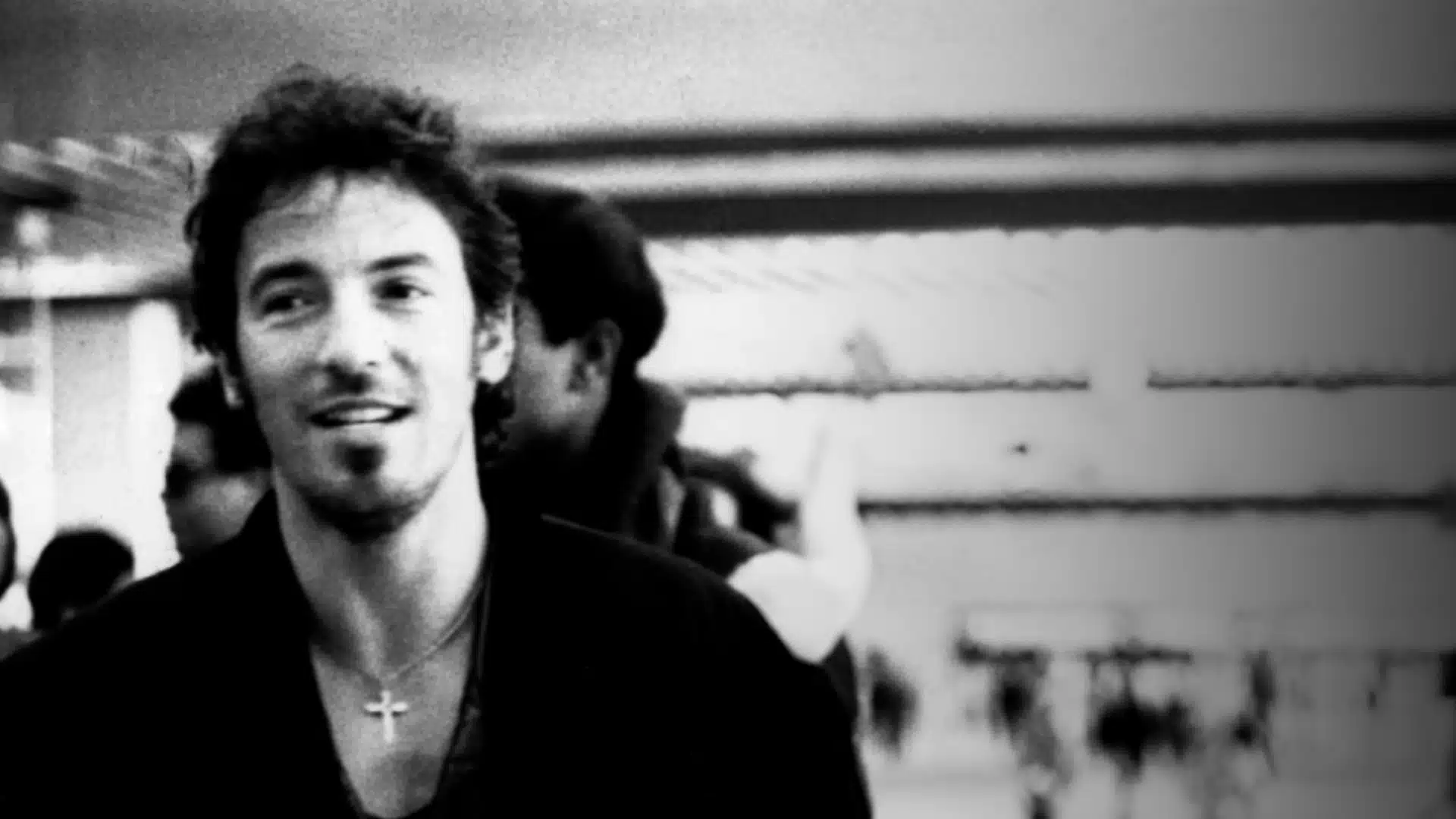 Black and white close up of Bruce Springsteen smiling backstage wearing necklace with cross pendant
