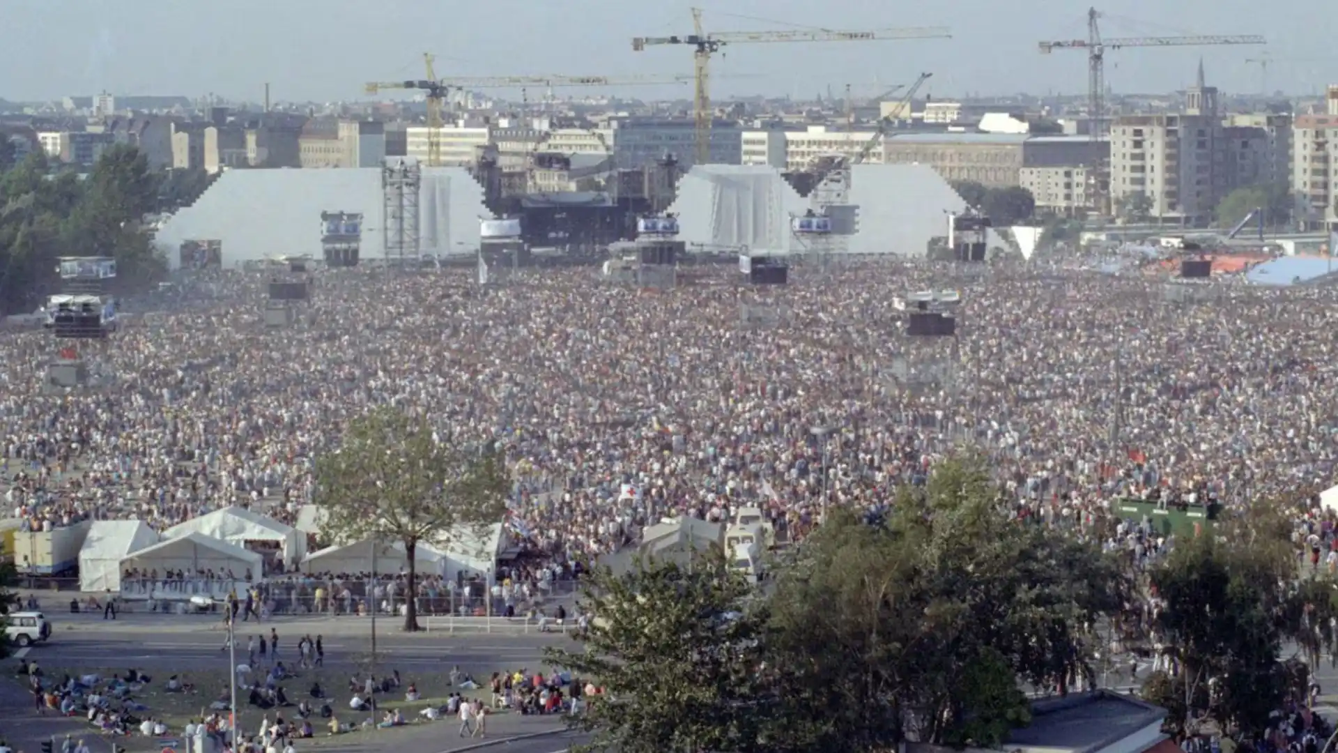 Huge crowd gathered at The Wall concert with large stage structures and city skyline in background view