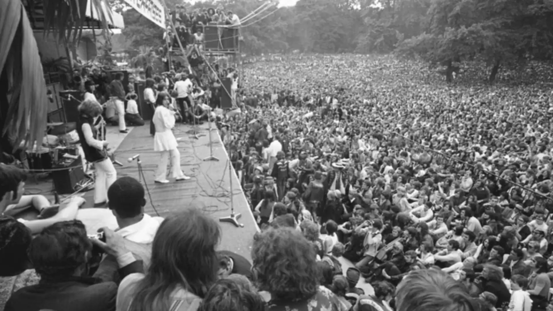 Black and white photo of band performing live on stage at Hyde Park with massive crowd stretching across park
