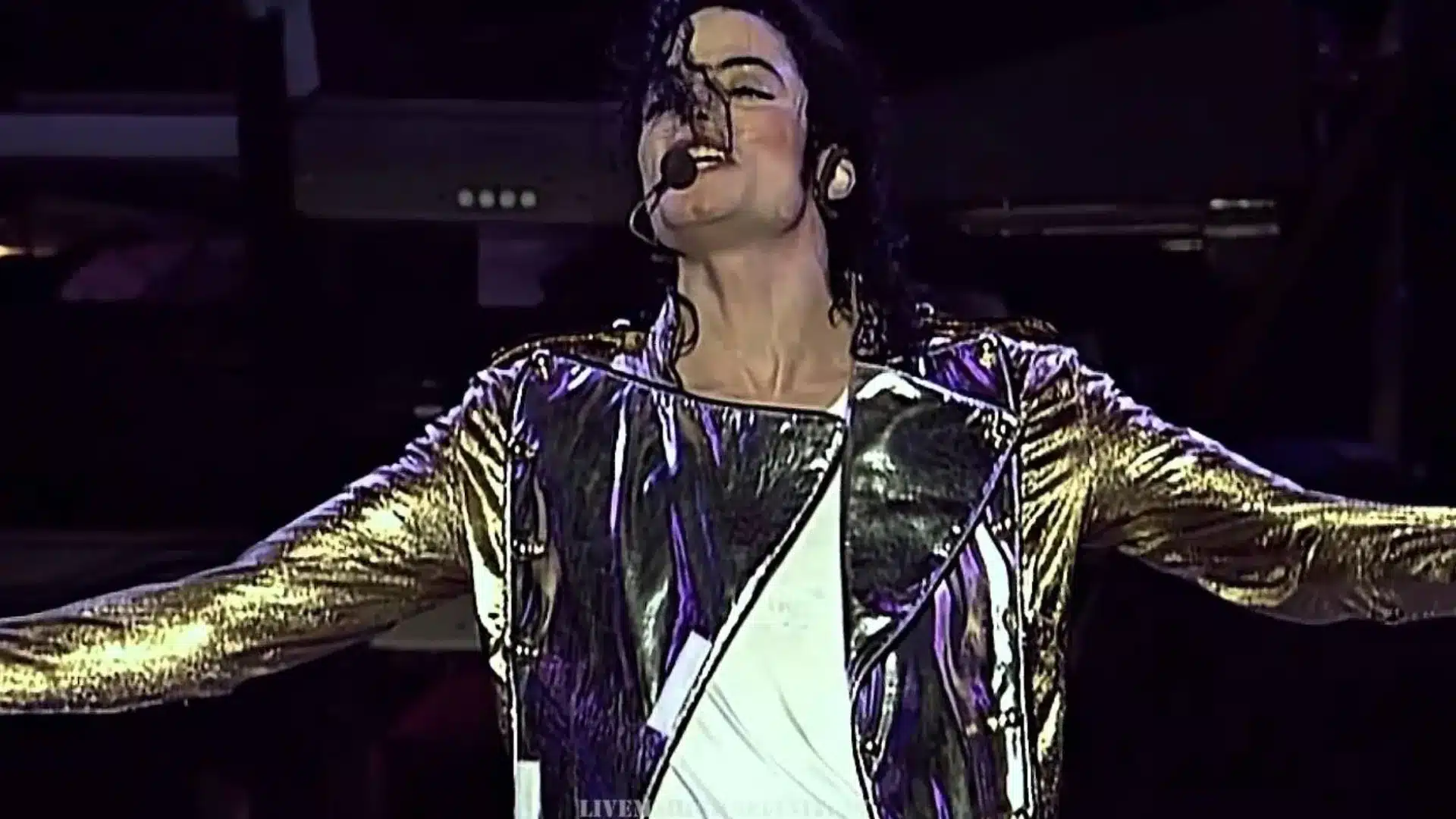 Michael Jackson performing live in metallic jacket singing with arms open under the stage lighting