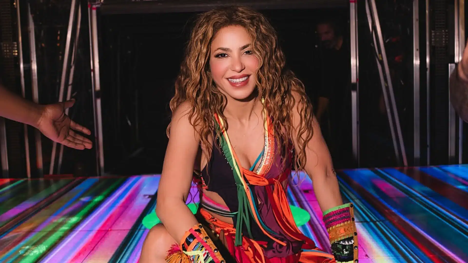 Shakira smiling on colorful stage wearing vibrant outfit during energetic live concert performance