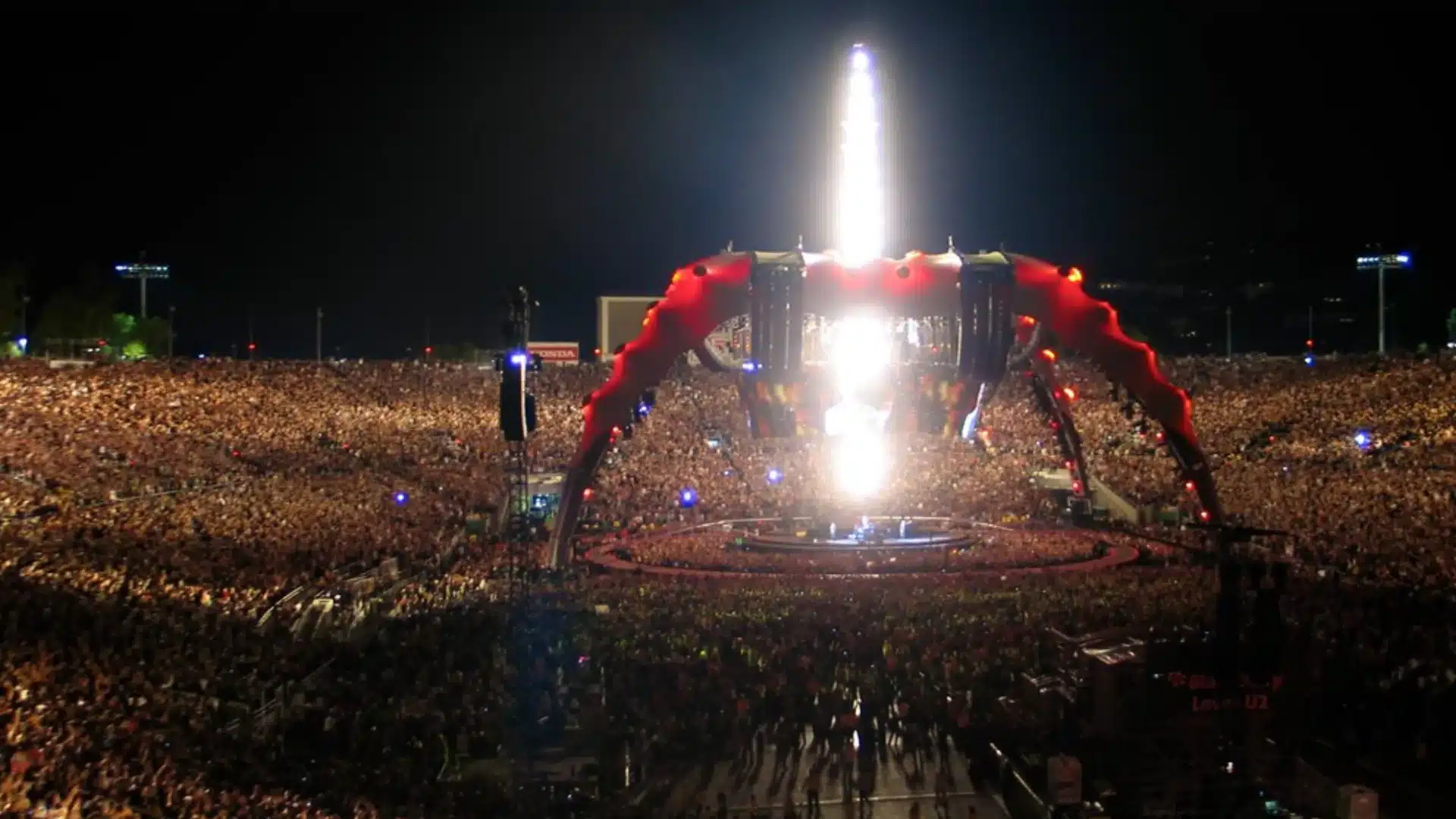 U2 performing at Rose Bowl stadium with giant claw stage and enormous crowd surrounding circular platform