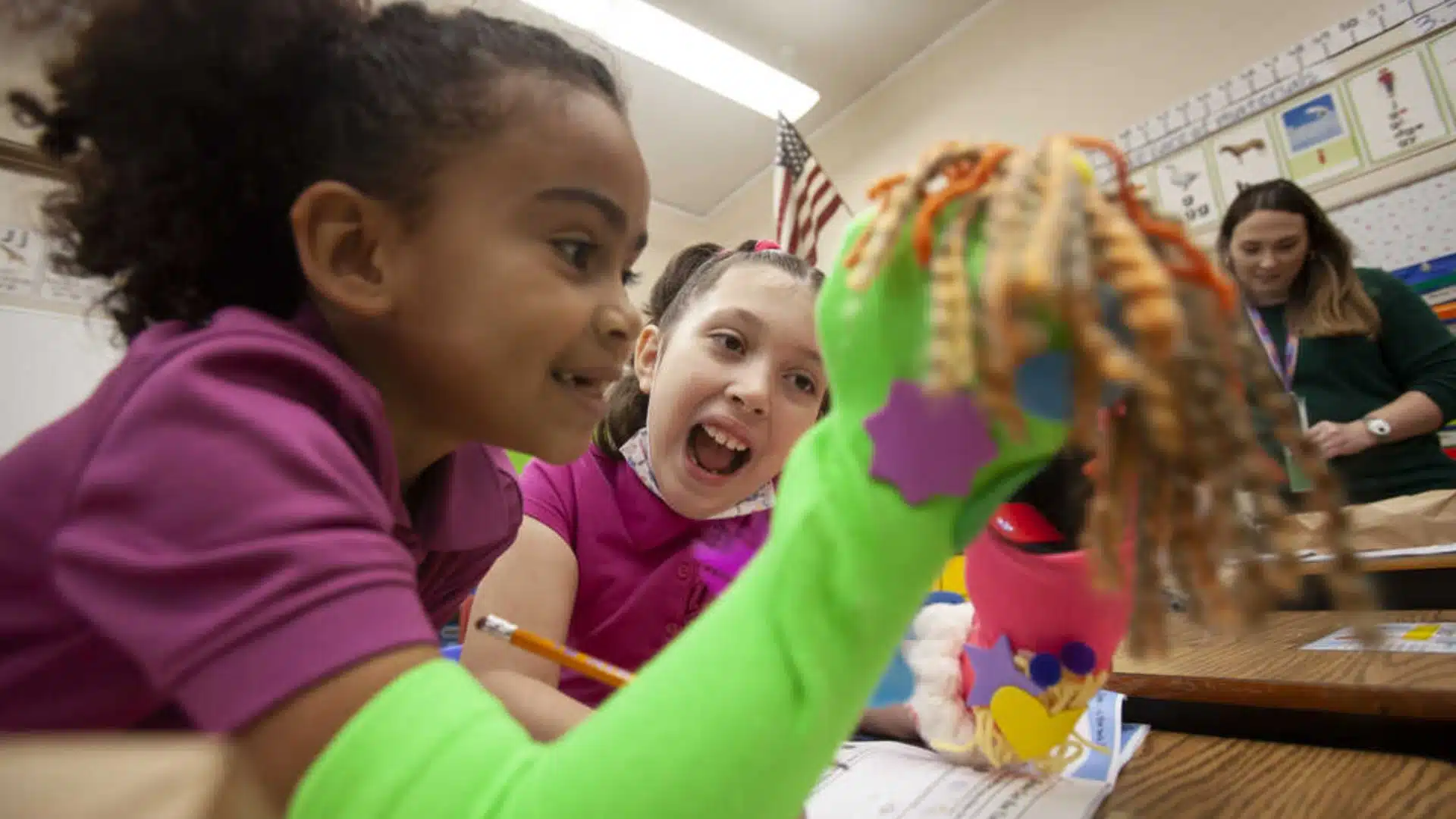 Kids playing with colorful handmade puppet in classroom, engaging in fun storytelling and creative skit activity