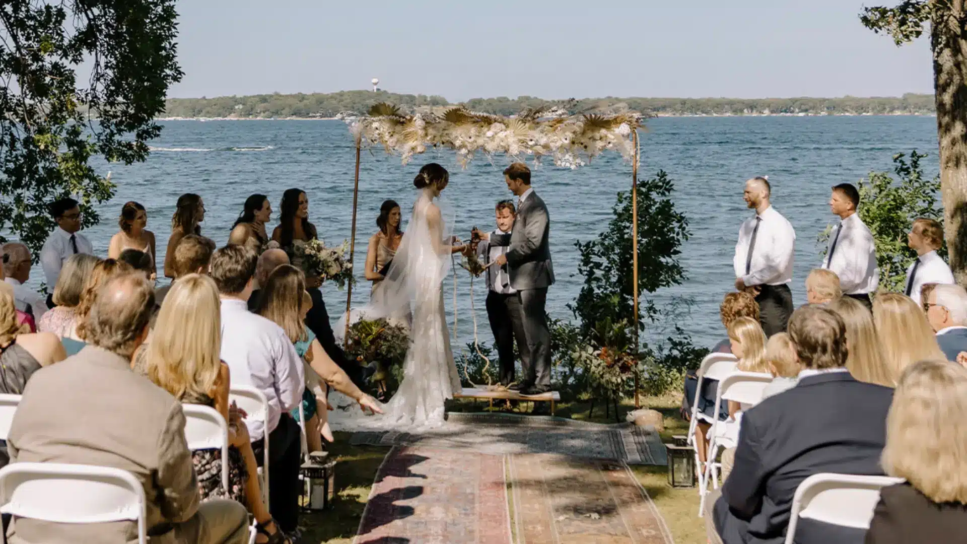 Outdoor wedding ceremony by lake with bride and groom exchanging vows in front of guests