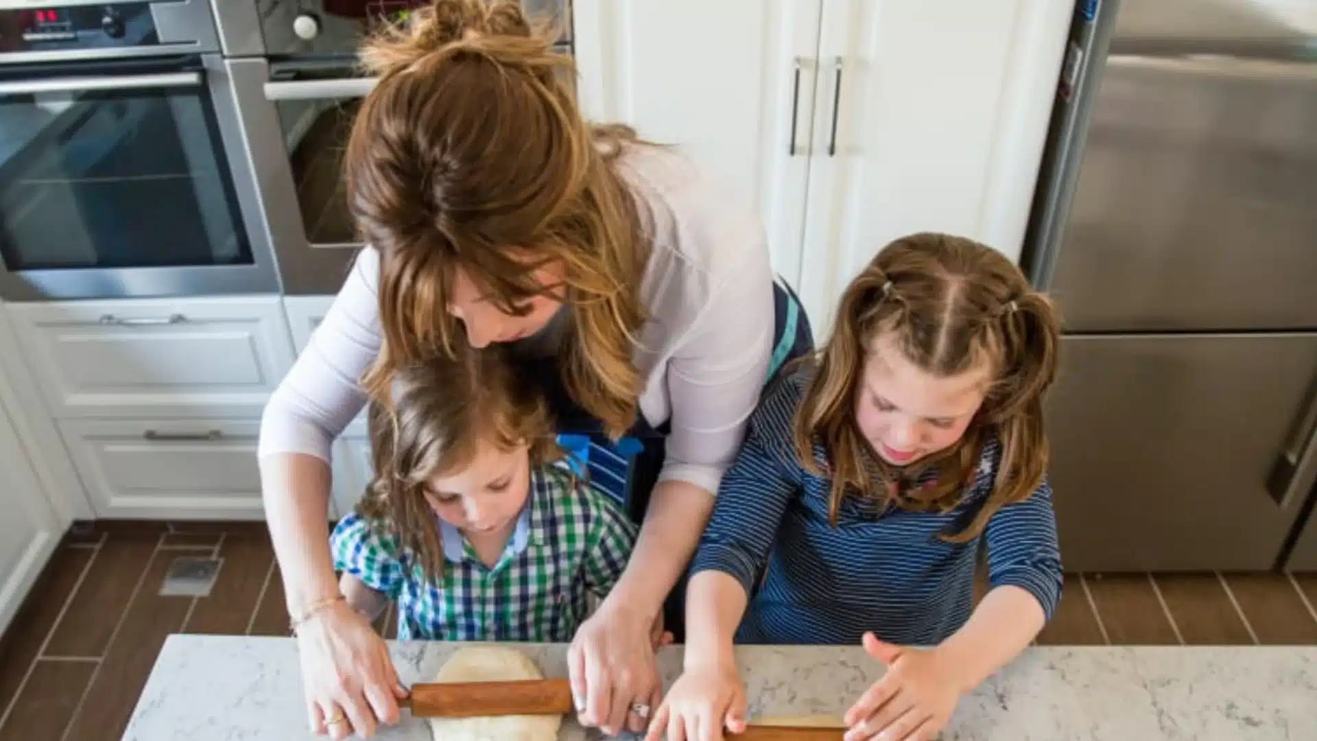 Parent and two children rolling dough together in kitchen, enjoying a cozy winter cooking activity at home