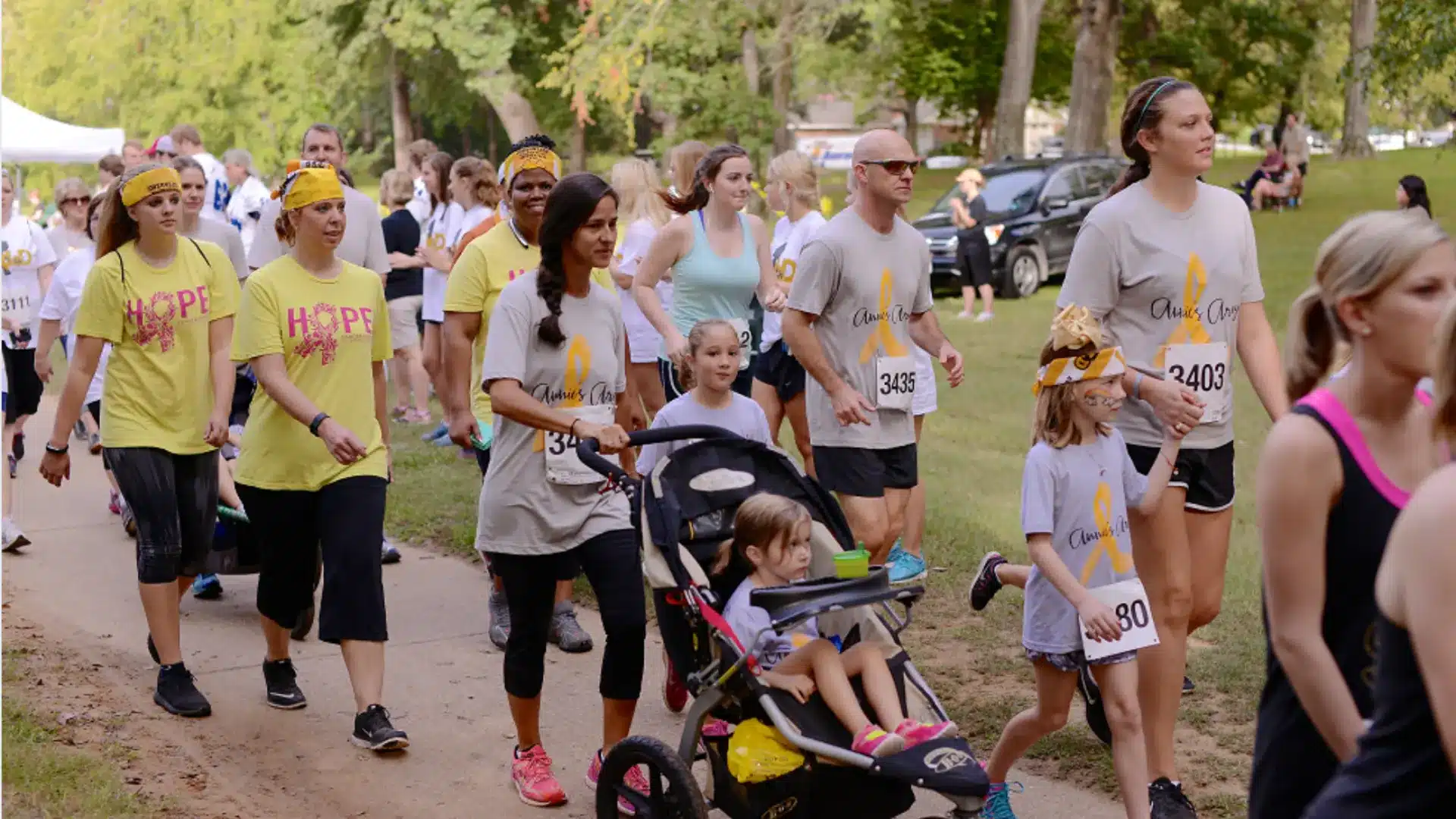 Participants walking together in charity walkathon event, wearing matching shirts and race numbers in park