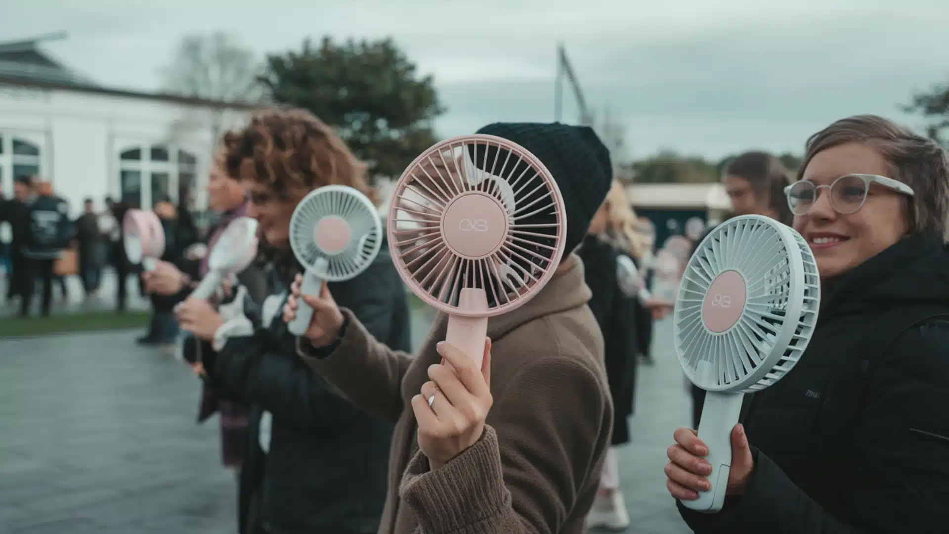 People holding portable handheld fans at outdoor event staying cool while standing in a casual group setting