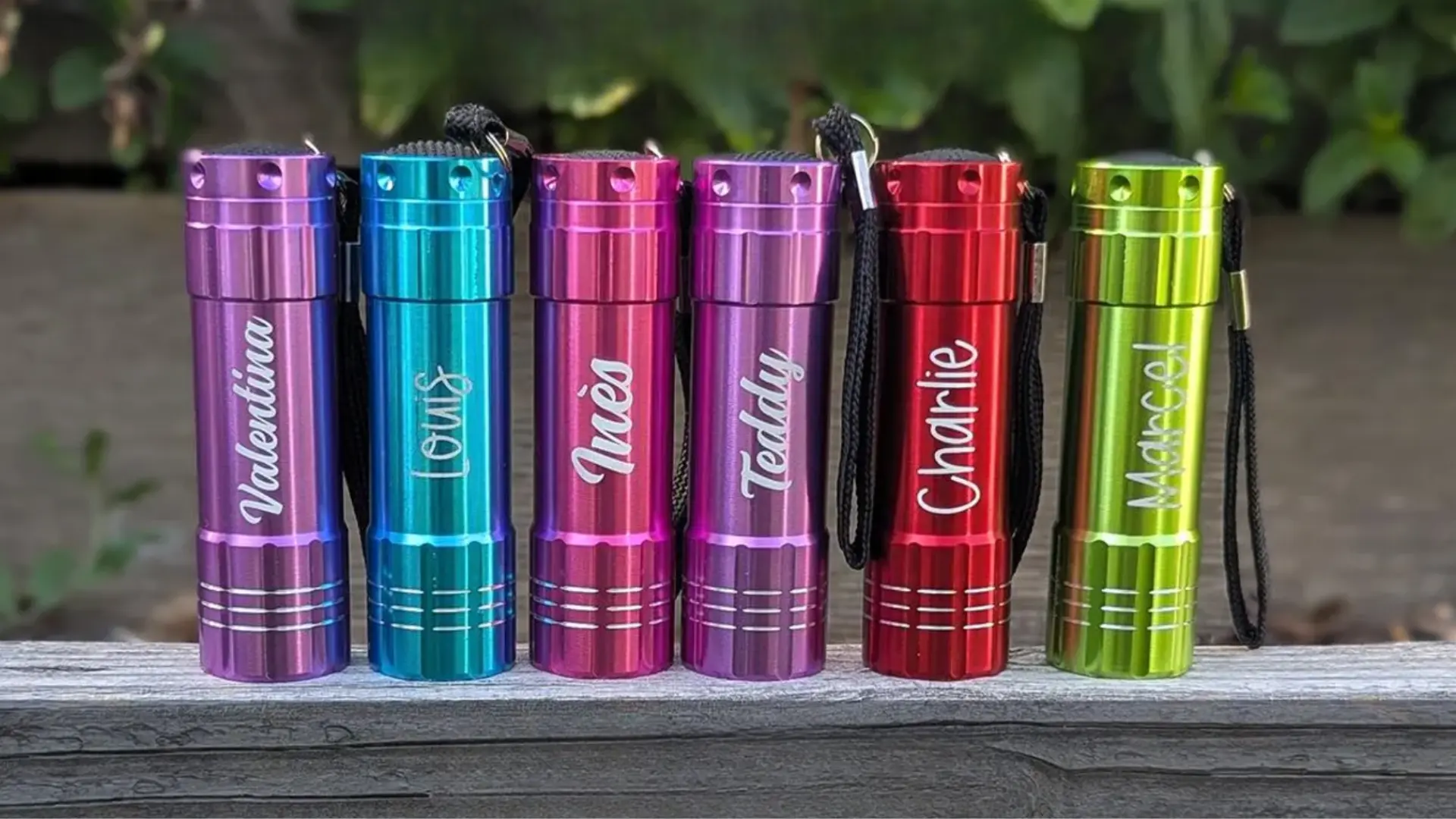 Personalized mini LED flashlights in bright colors with engraved names displayed in a neat row