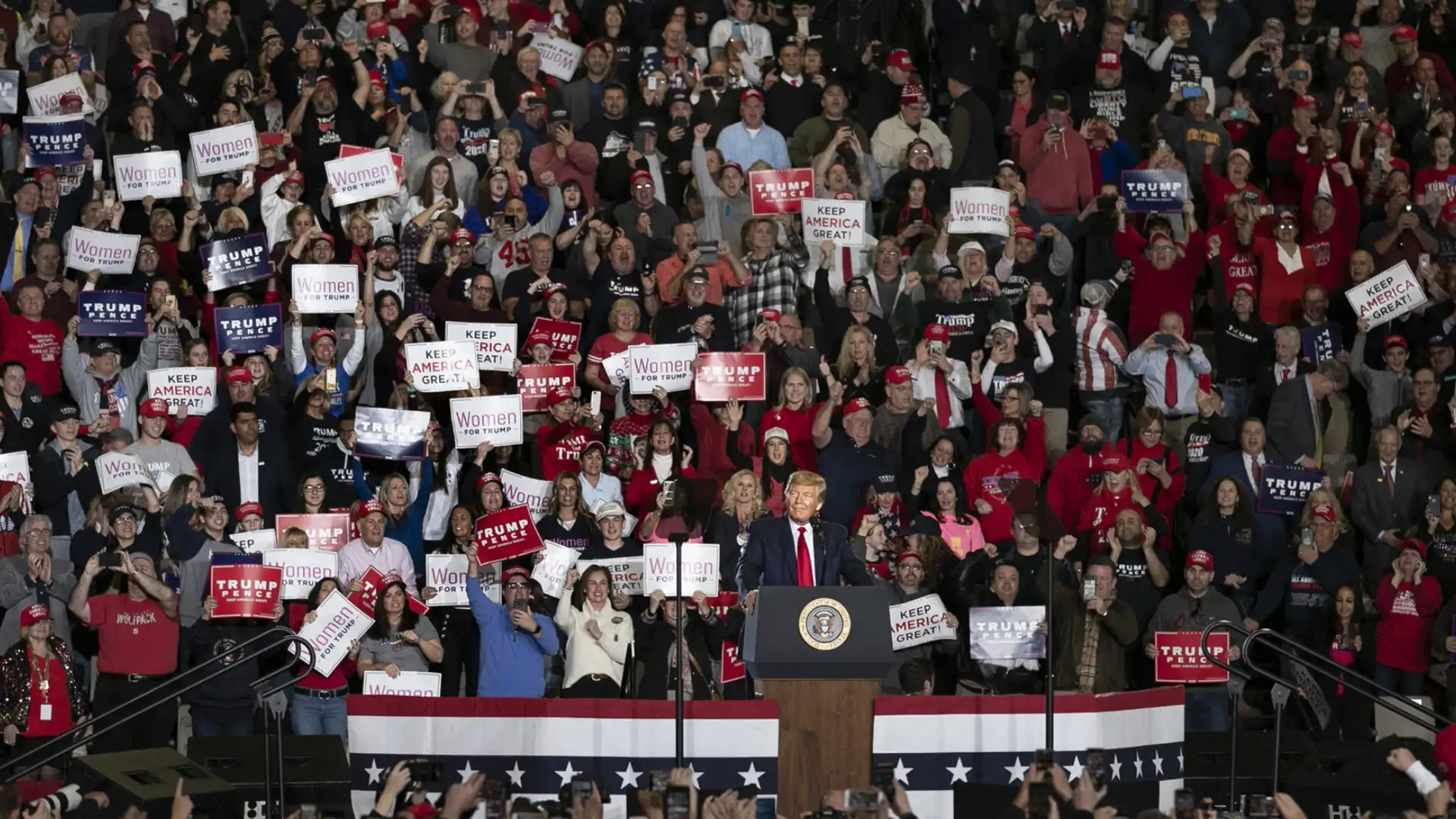 Political rally with speaker at podium and crowd holding signs, cheering during campaign event