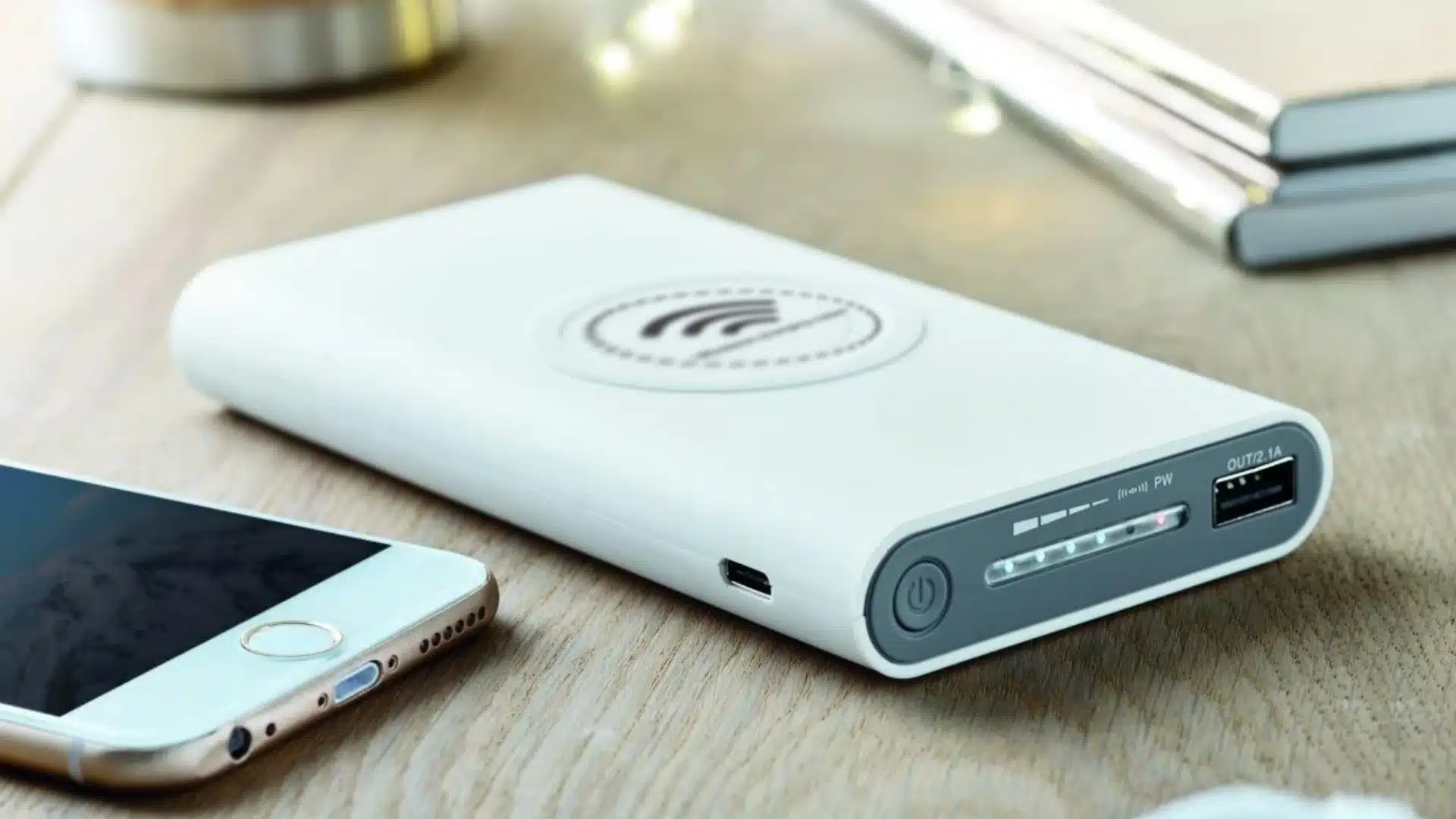 Portable power bank with LED battery indicator and USB port placed beside smartphone on wooden desk