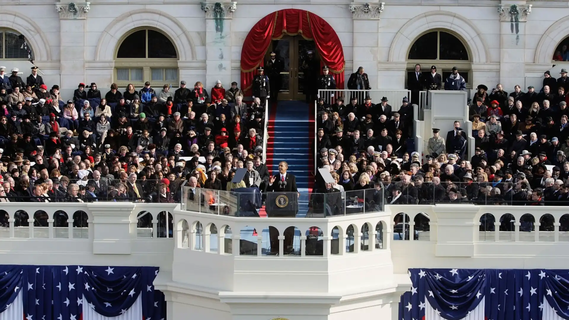 Presidential inauguration ceremony with speaker at podium addressing large crowd outside historic building