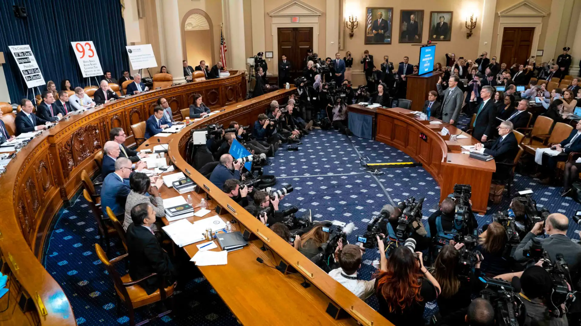 Public hearing in government chamber with officials, media, and audience during formal proceedings