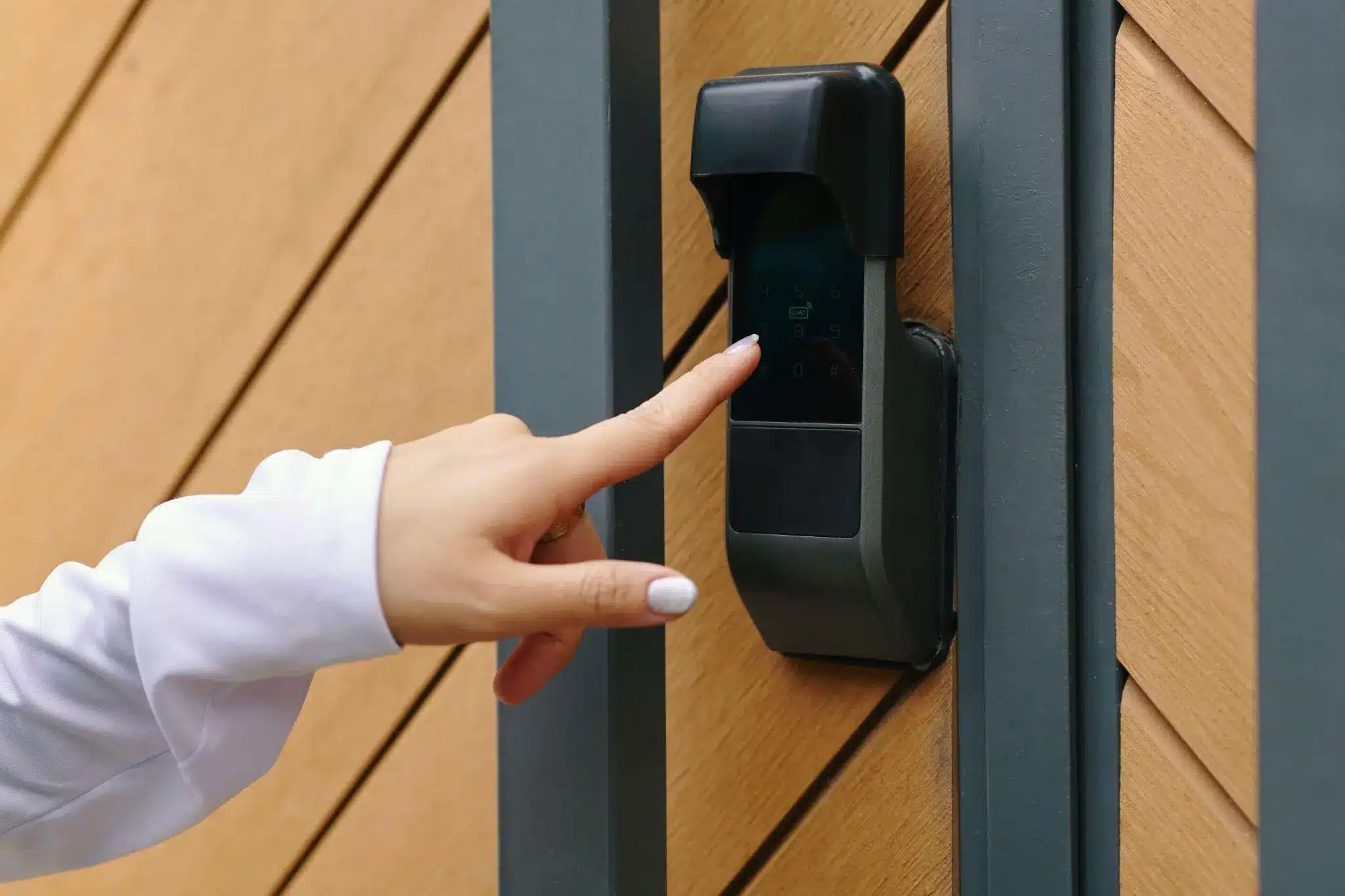Person pressing numeric keypad on modern door with wood paneling and gray frame