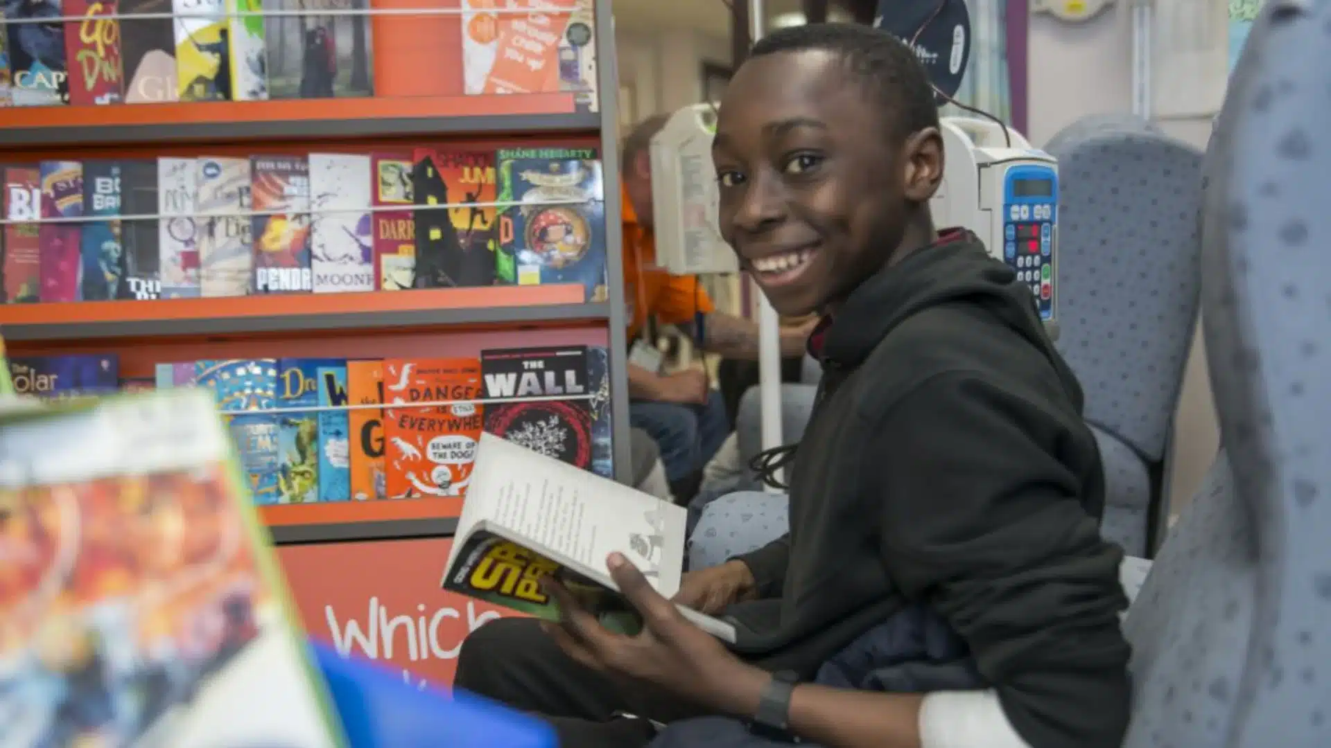 Student reading book in library aisle, smiling during engaging read-a-thon school literacy event