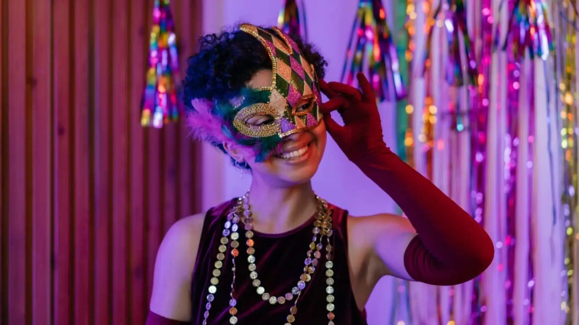 Student smiling in colorful masquerade mask with festive decorations, celebrating themed homecoming event