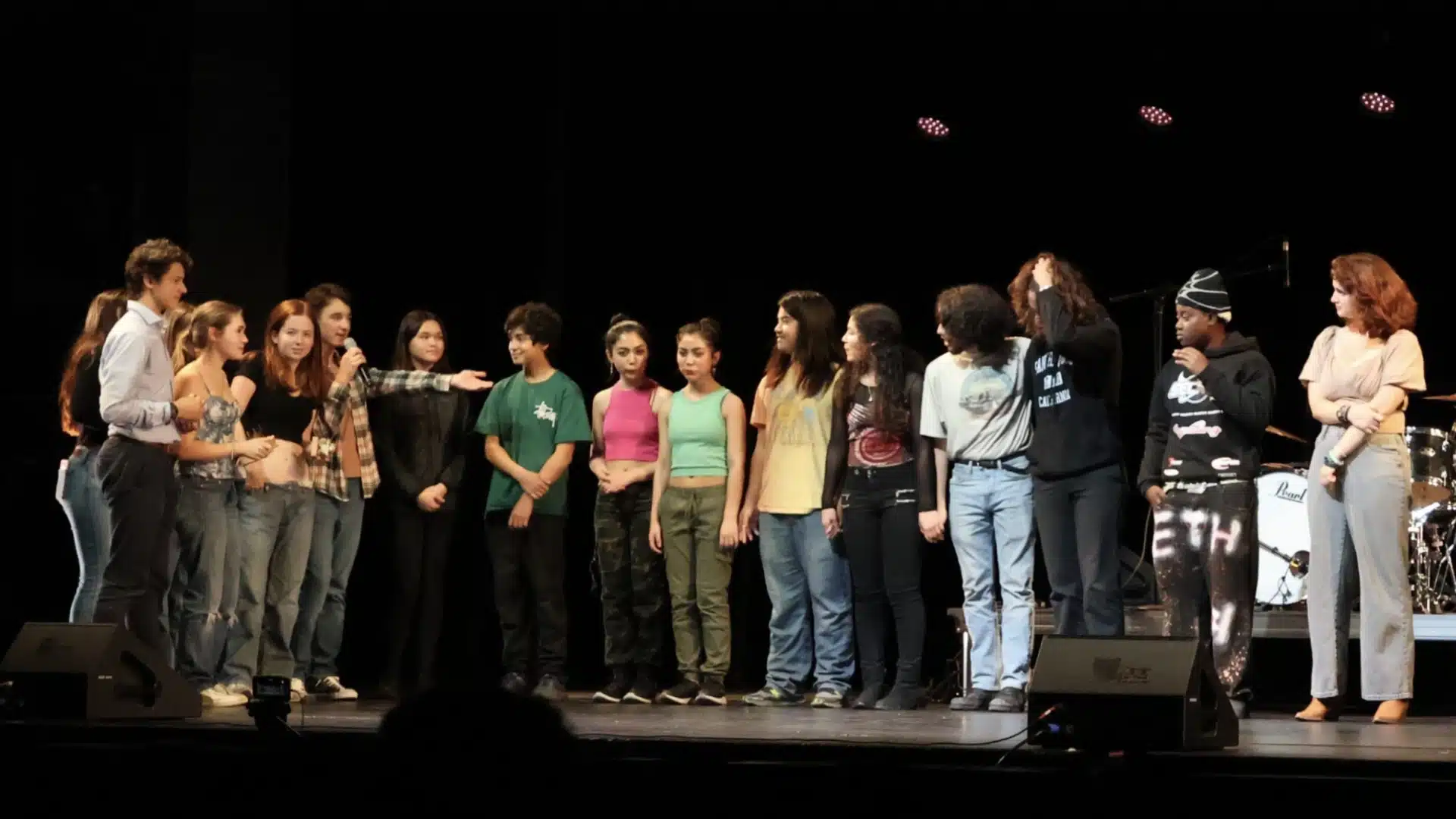 Students gathered on stage during a school talent show, performing and engaging with an audience in a lively setting