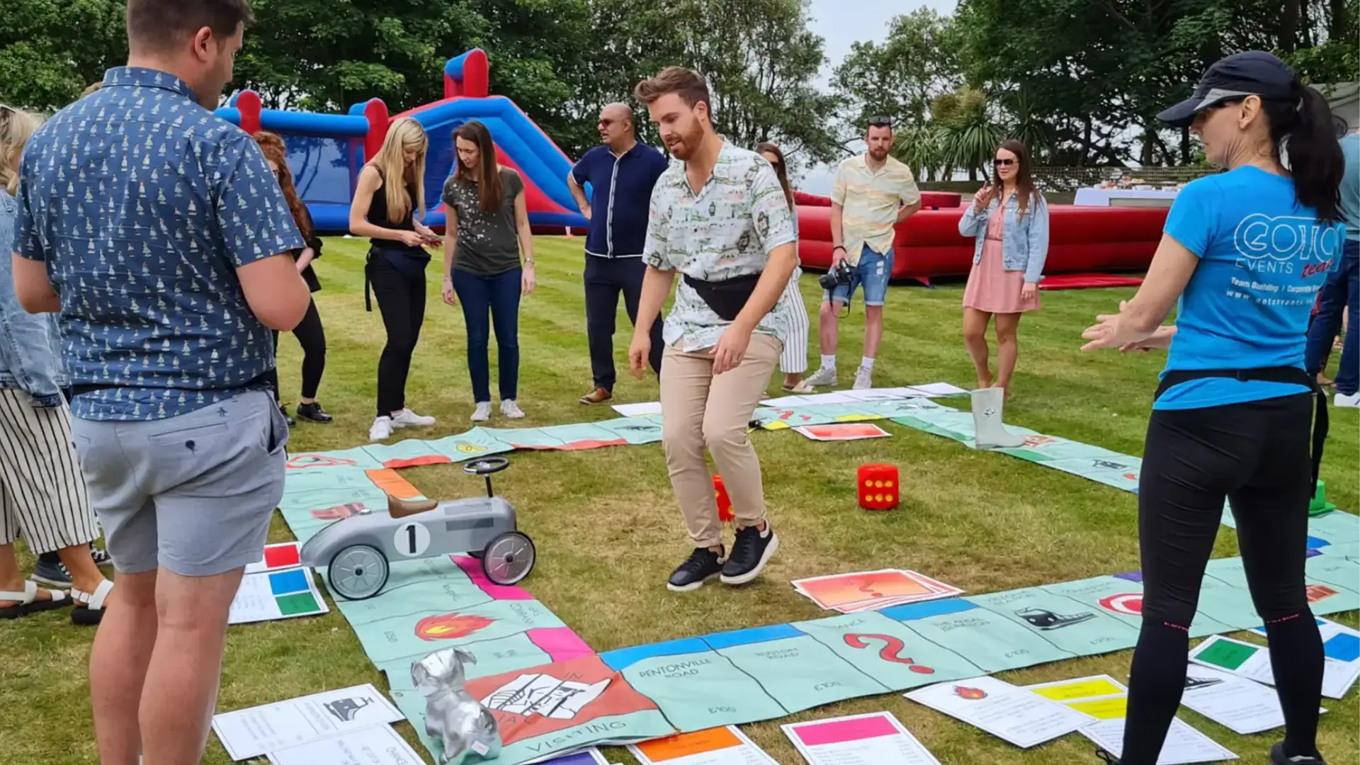 Team building event outdoors with group playing giant board game on grass with inflatable activities nearby