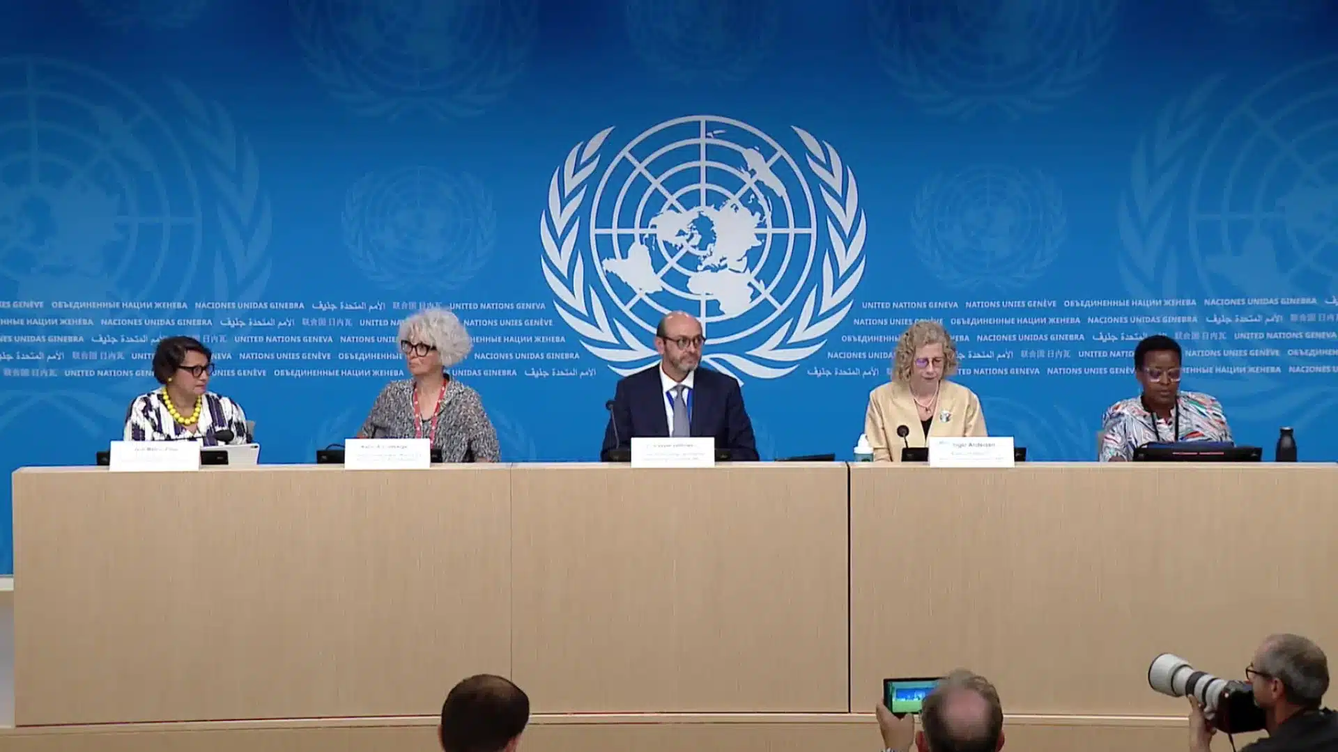 United Nations press conference panel with speakers seated at table addressing media in formal briefing room
