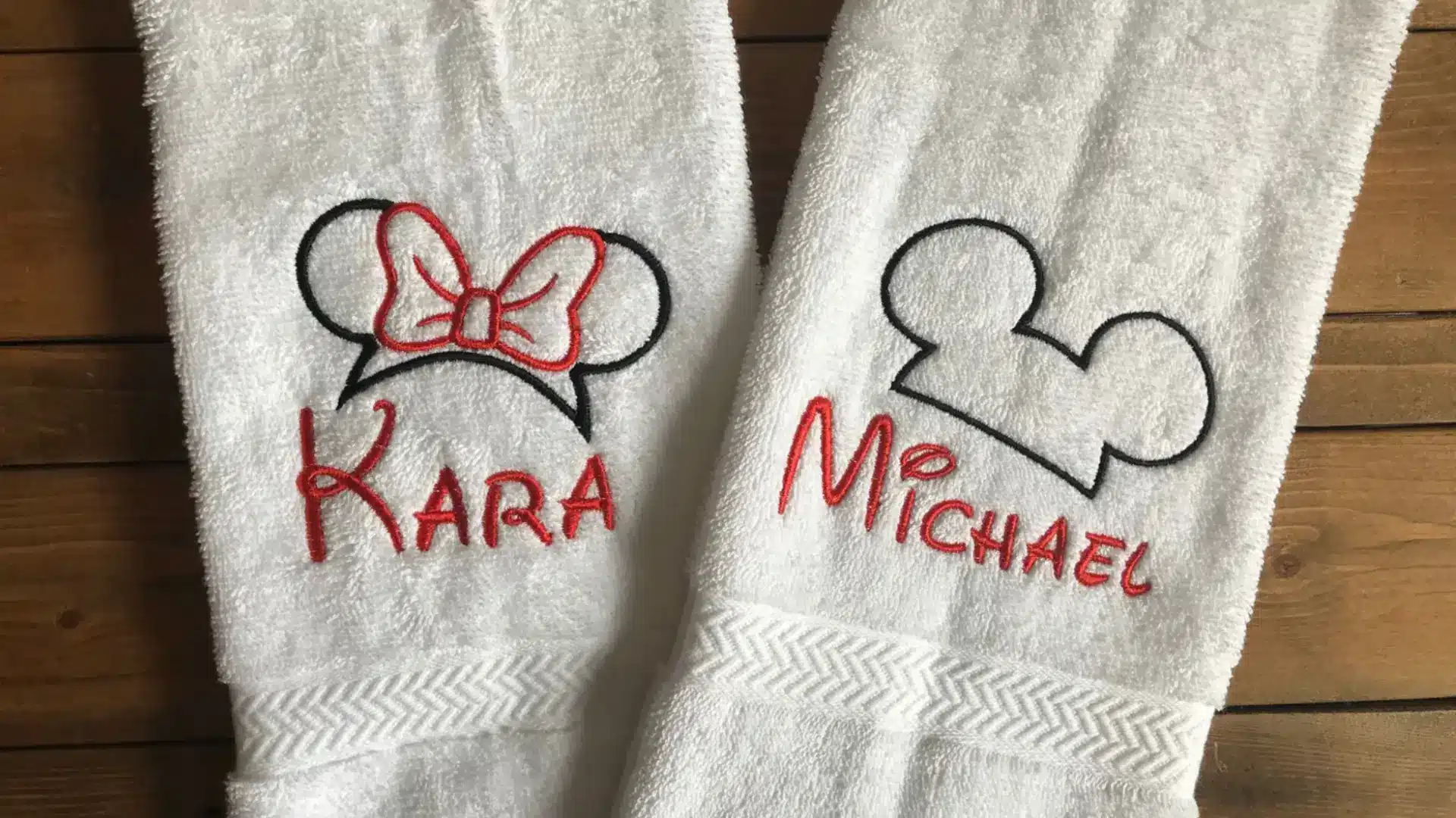 White personalized towels with embroidered names and cartoon ear designs neatly placed on wooden surface