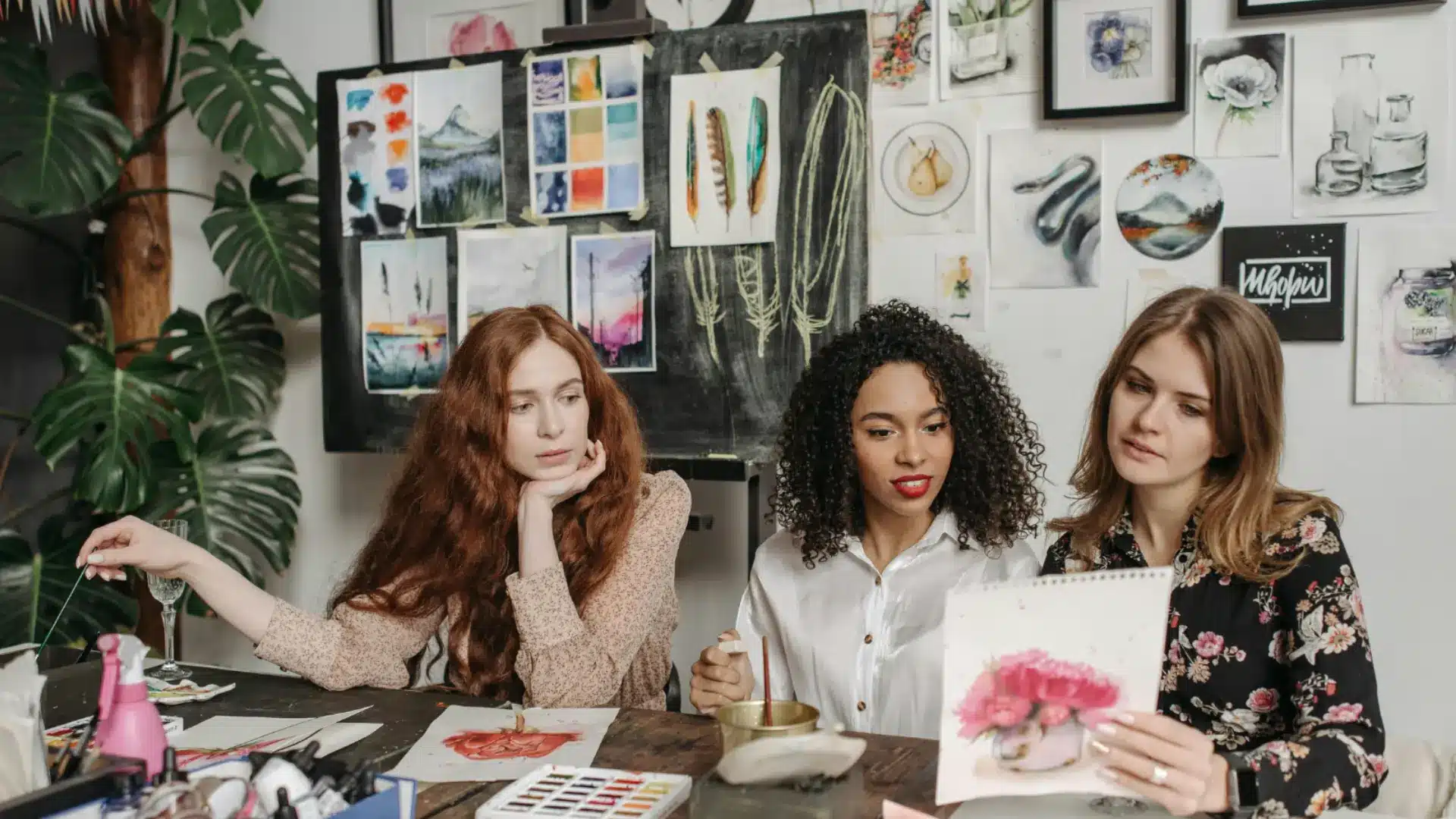 Women creating watercolor art together in cozy studio surrounded by paintings and creative supplies