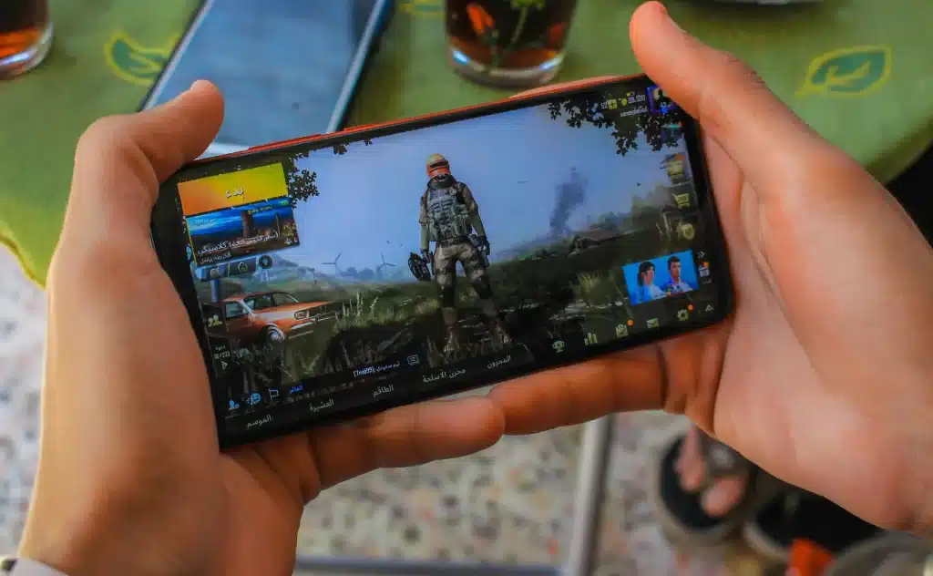 Hands holding smartphone displaying video game character selection screen in bright indoor setting