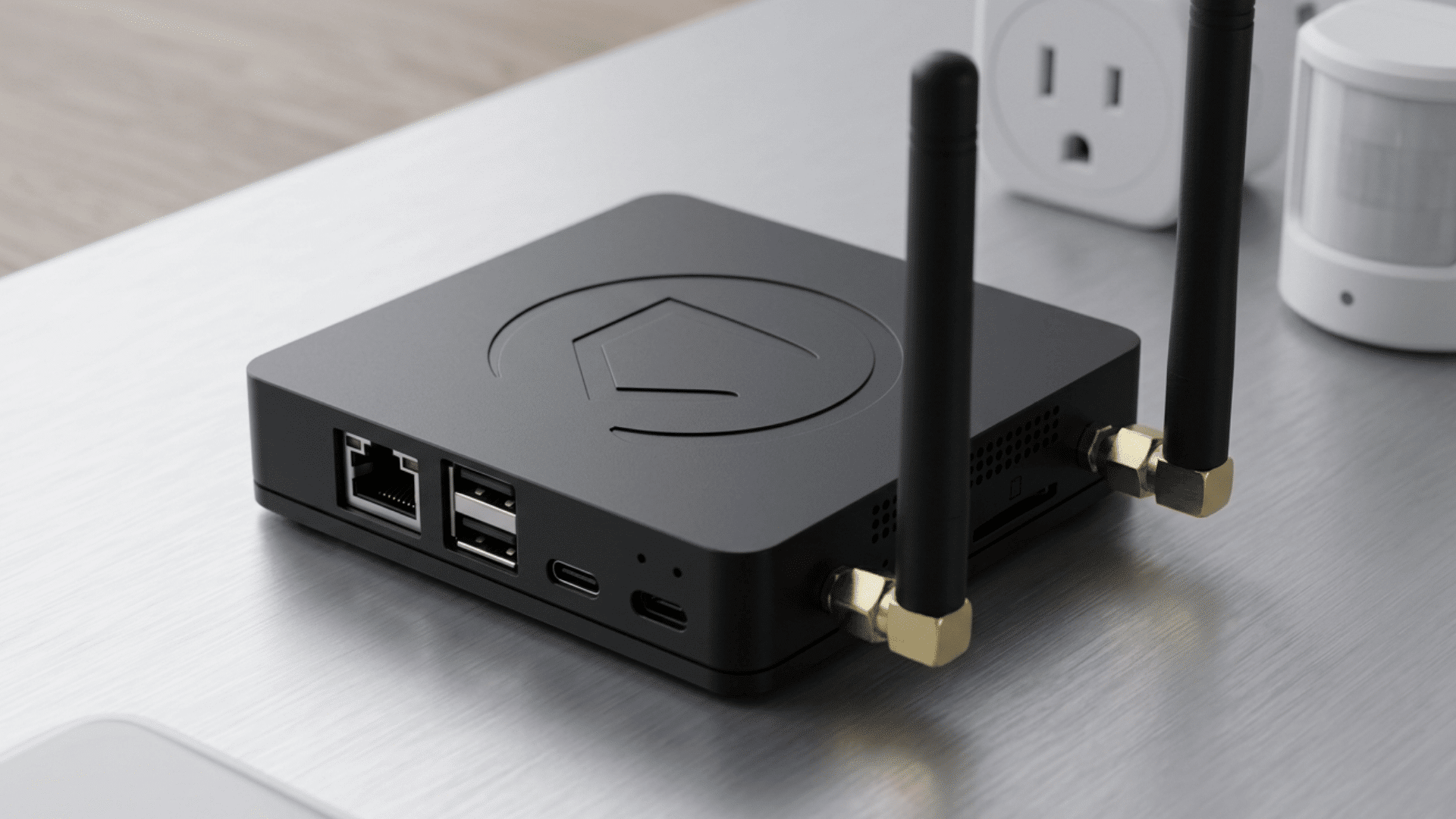A black smart home hub with dual antennas on a table surrounded by smart plugs and sensors