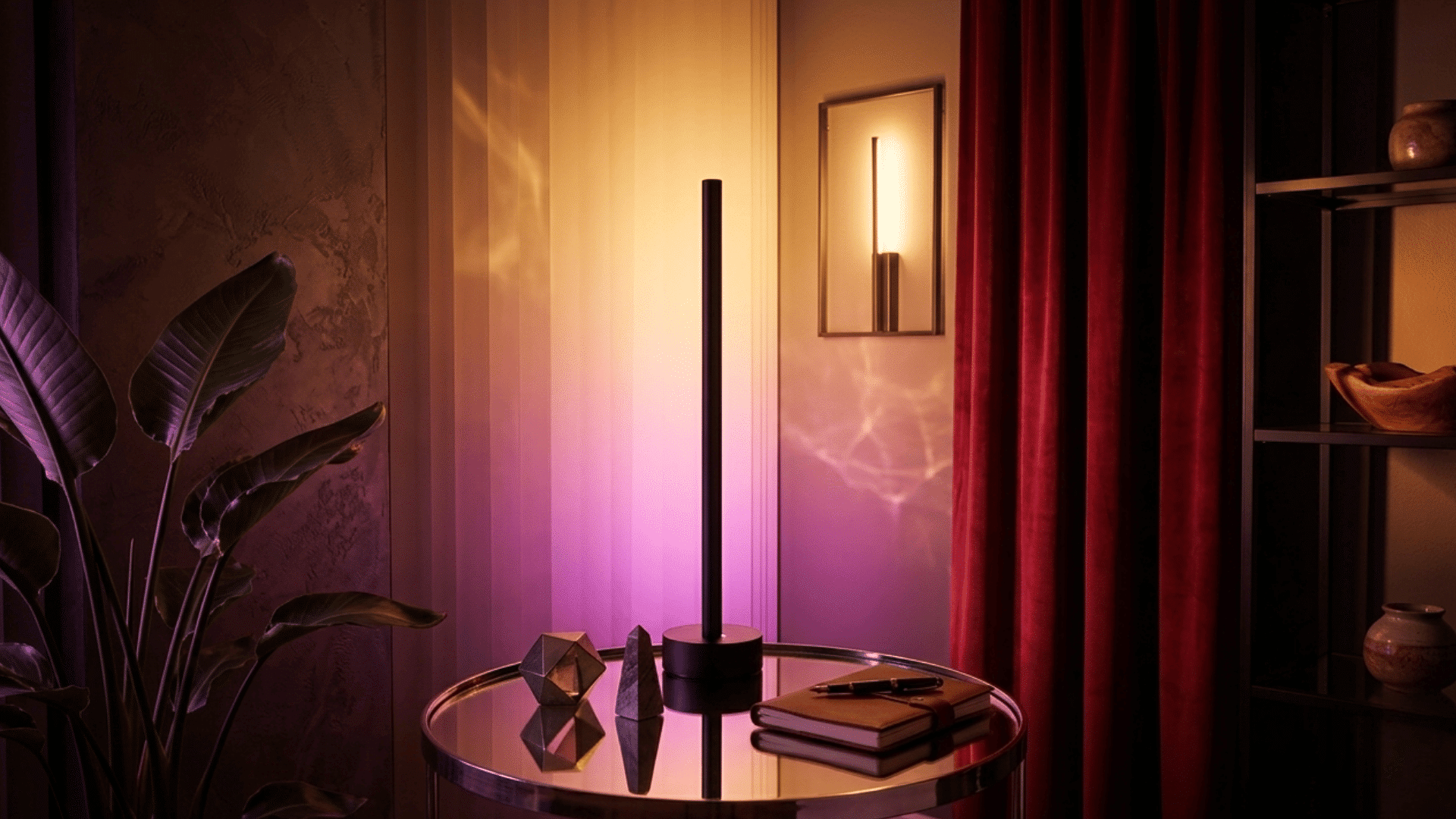 A modern lamp on a round glass table with geometric decor books and a plant casting purple and warm light