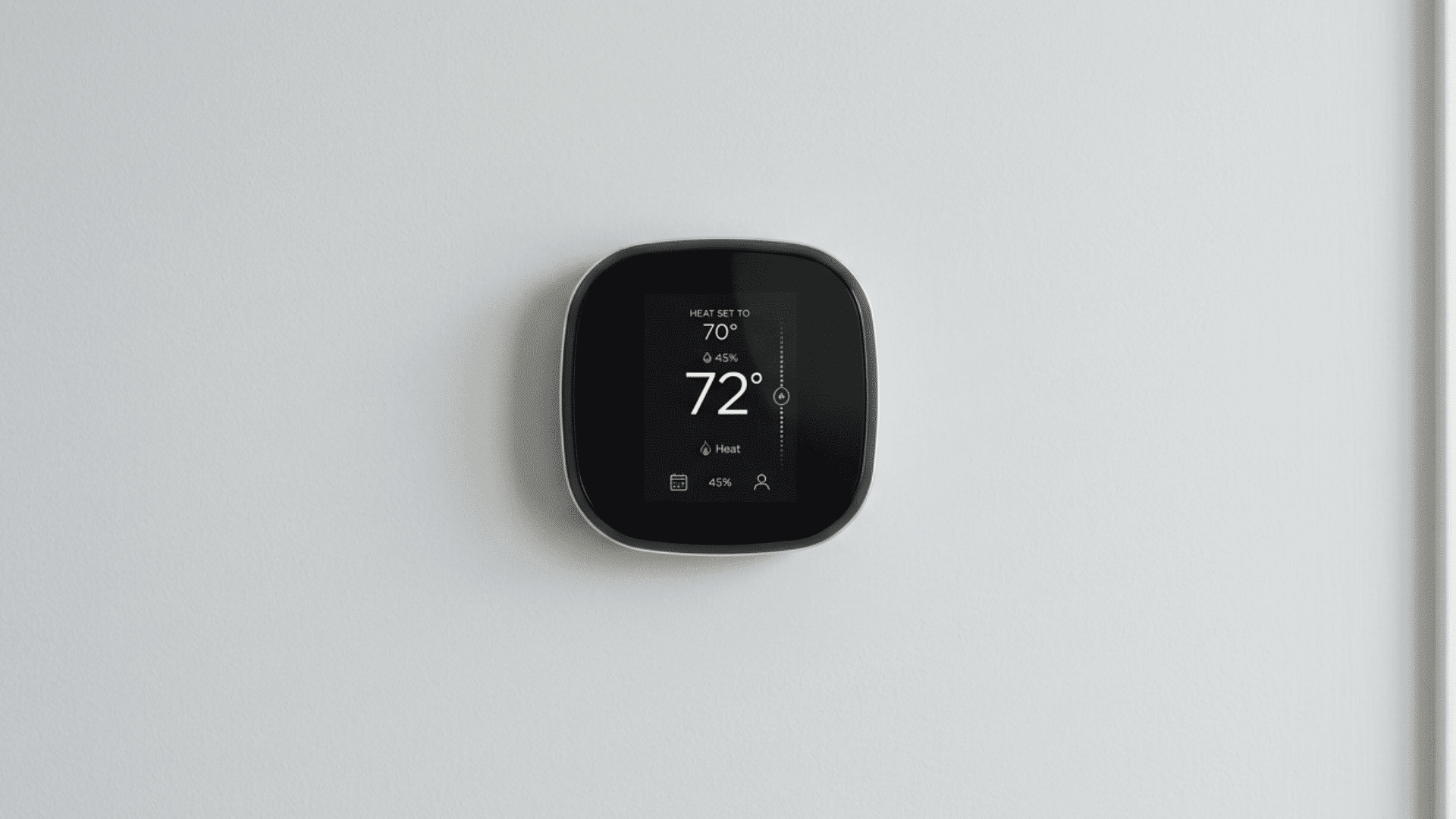 A smart thermostat mounted on a plain wall showing the current temperature and heat settings
