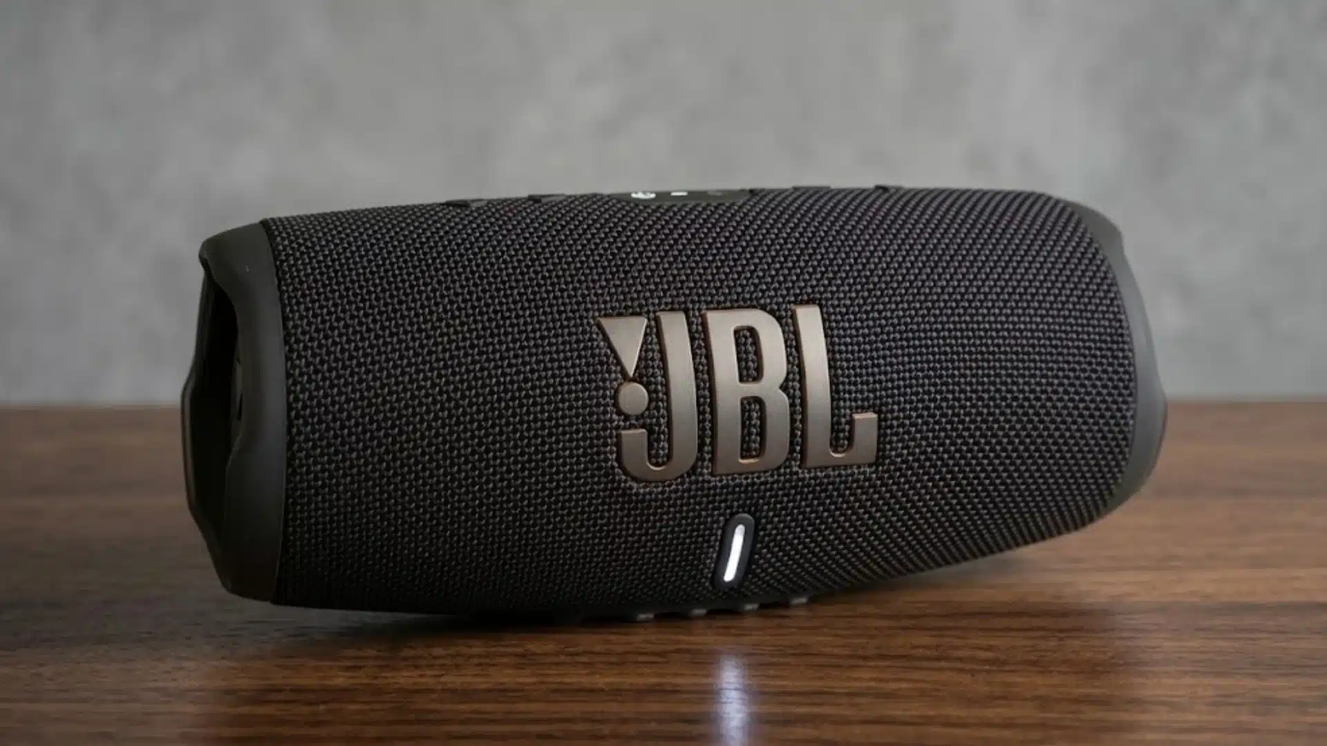 Black JBL Charge 5 portable Bluetooth speaker placed on a wooden surface with textured grille