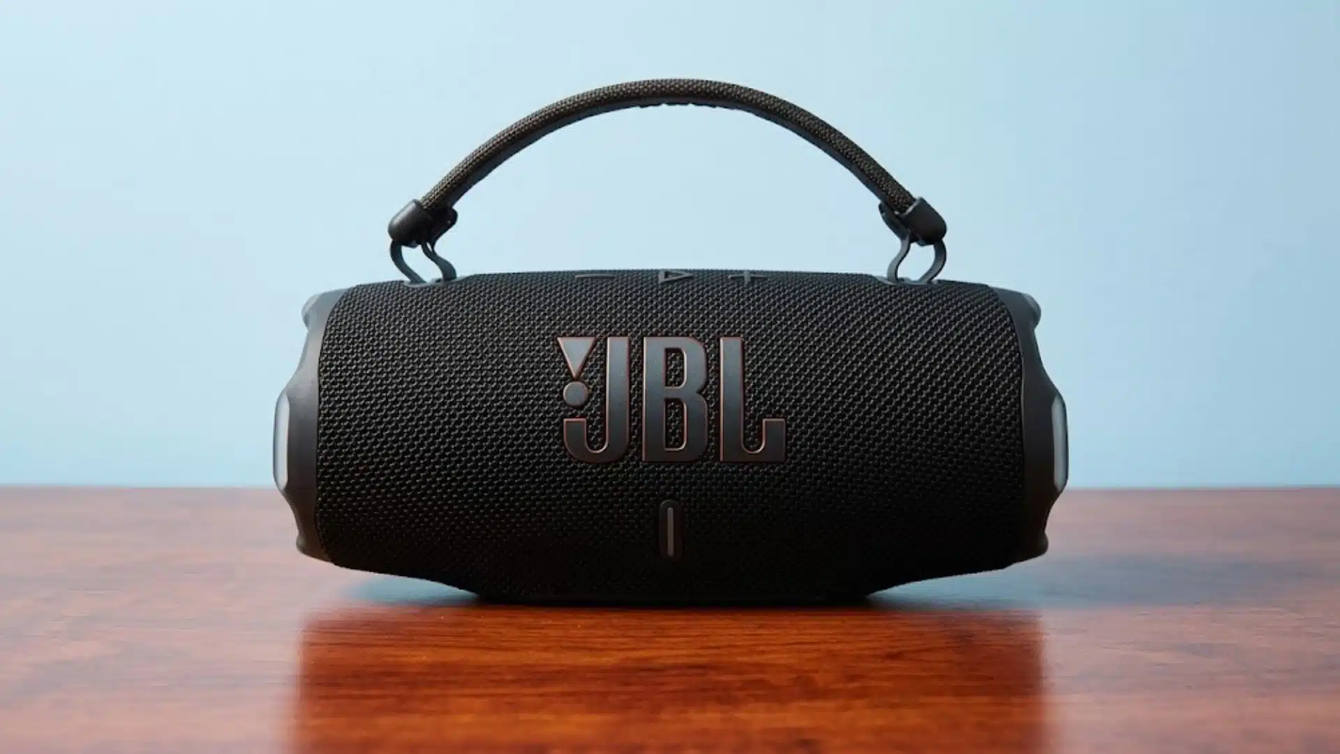 Black JBL Charge 6 portable Bluetooth speaker with handle, placed on wooden surface against blue wall